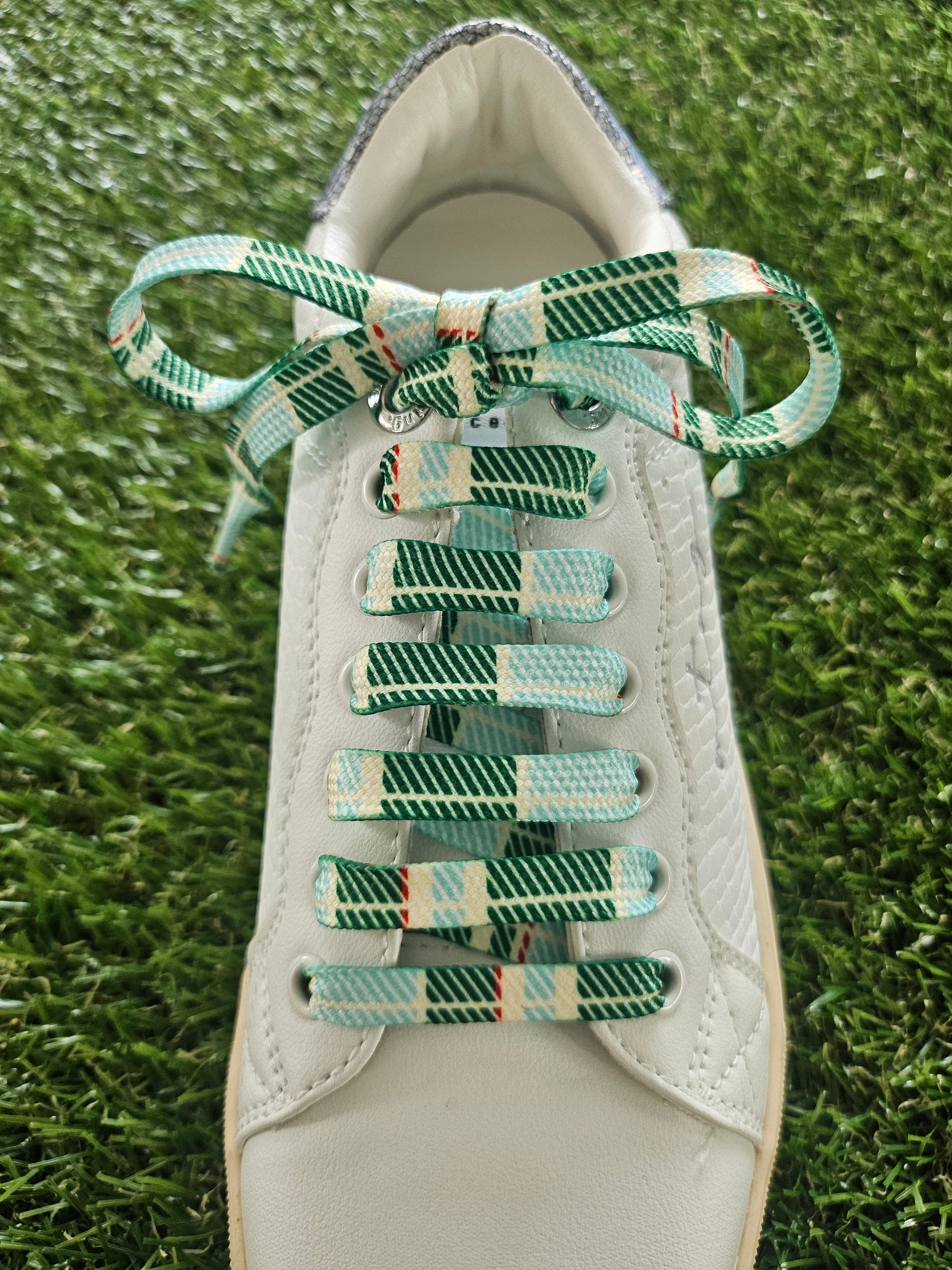White sneaker with green and white checkered laces on a grass background