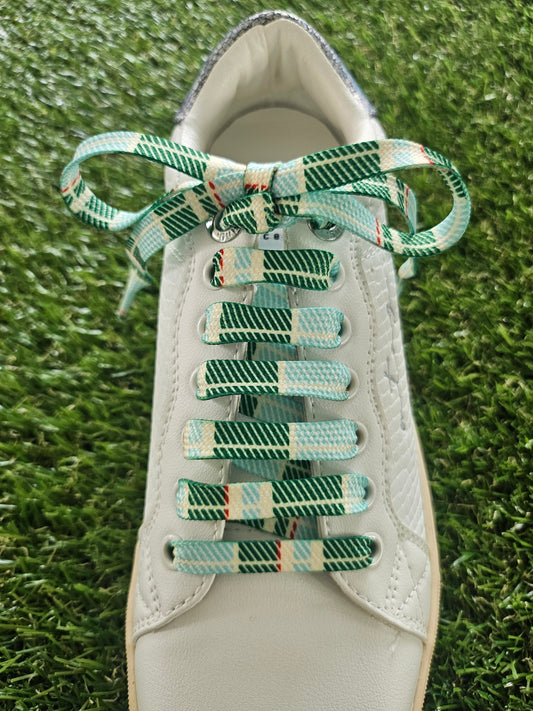 White sneaker with green and white checkered laces on a grass background
