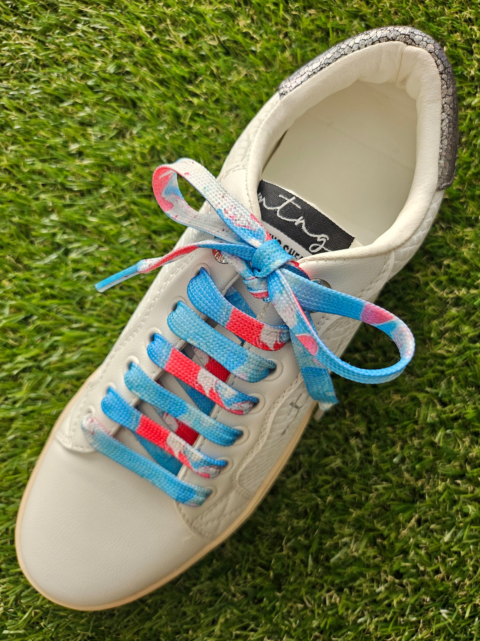 White sneaker with colorful laces on a grass background
