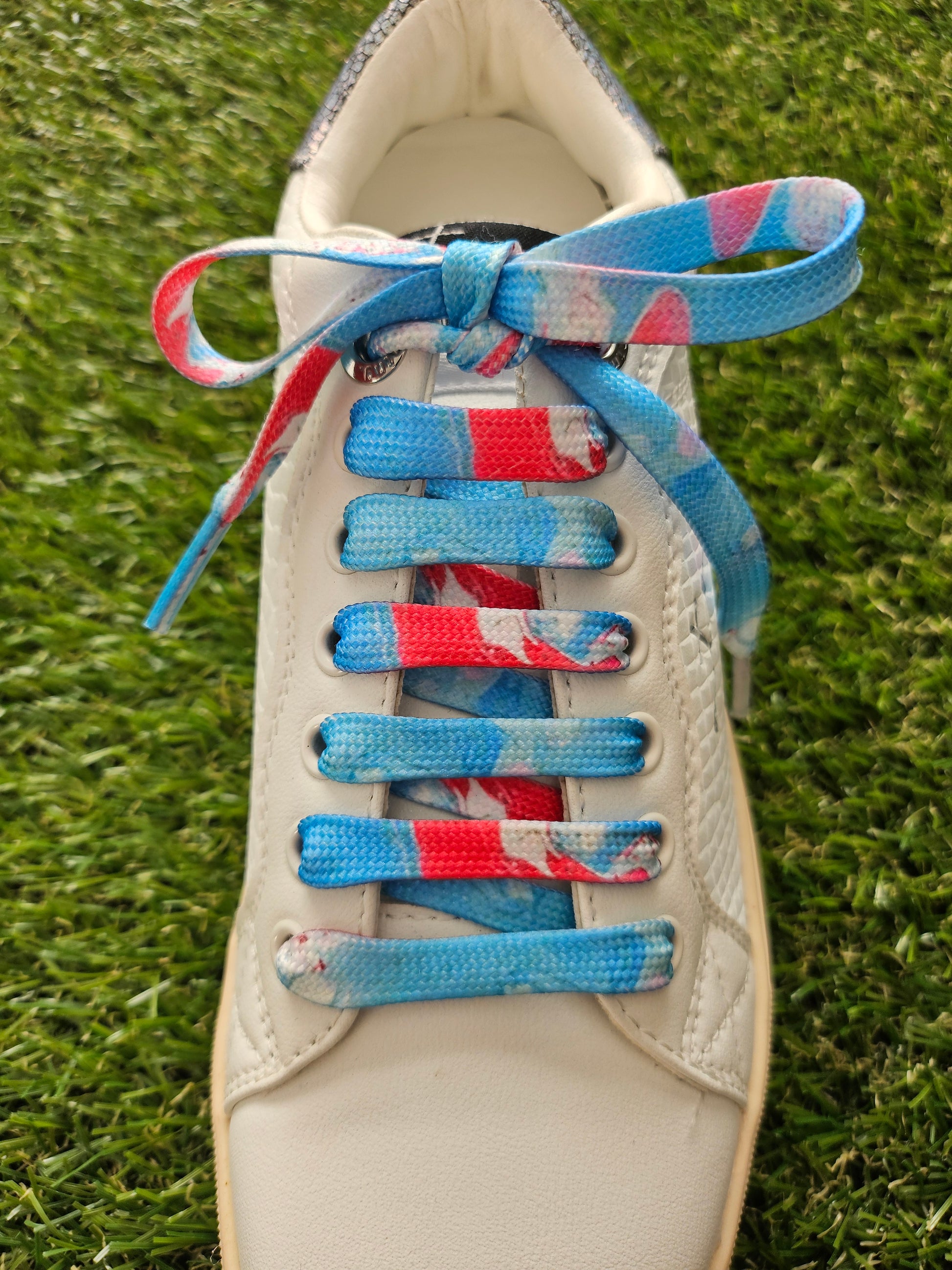White sneaker with colorful laces on a grass background