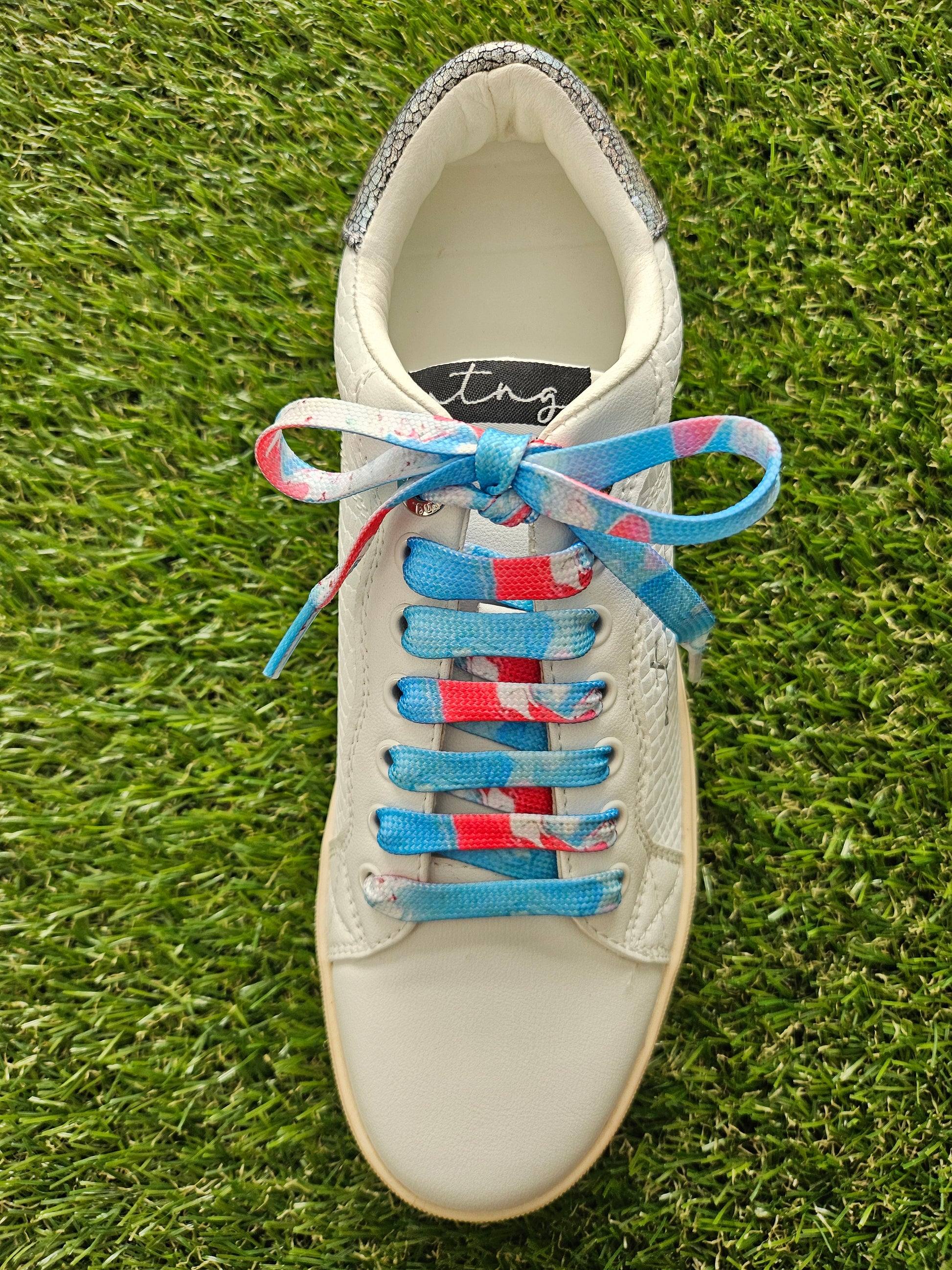 White sneaker with colorful laces on a grass background