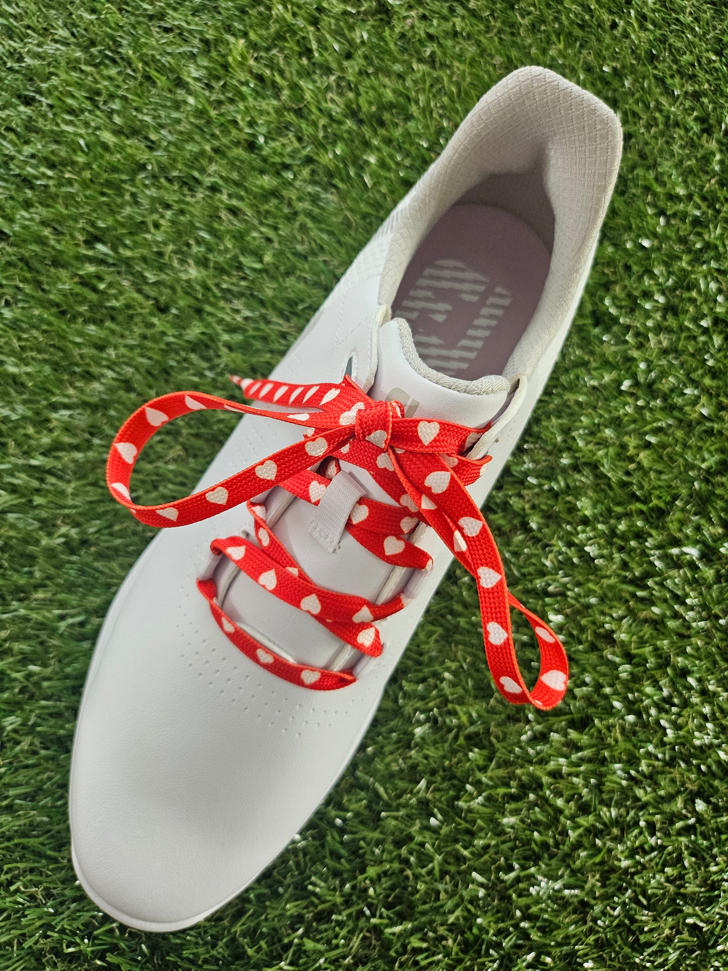 White ladies golf shoe with red and white laces on a grass background