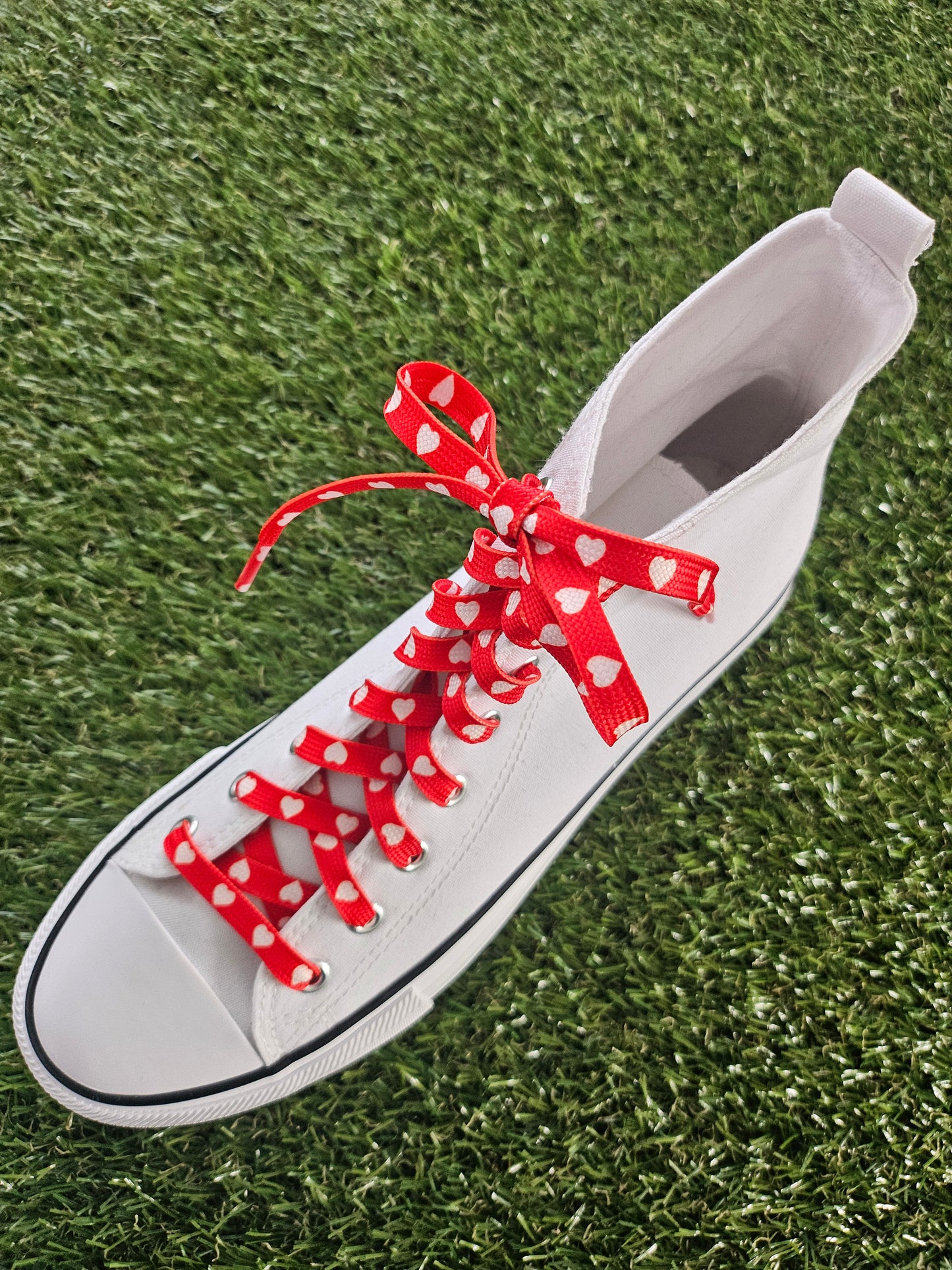 White sneaker with red and white heart laces on a grass background