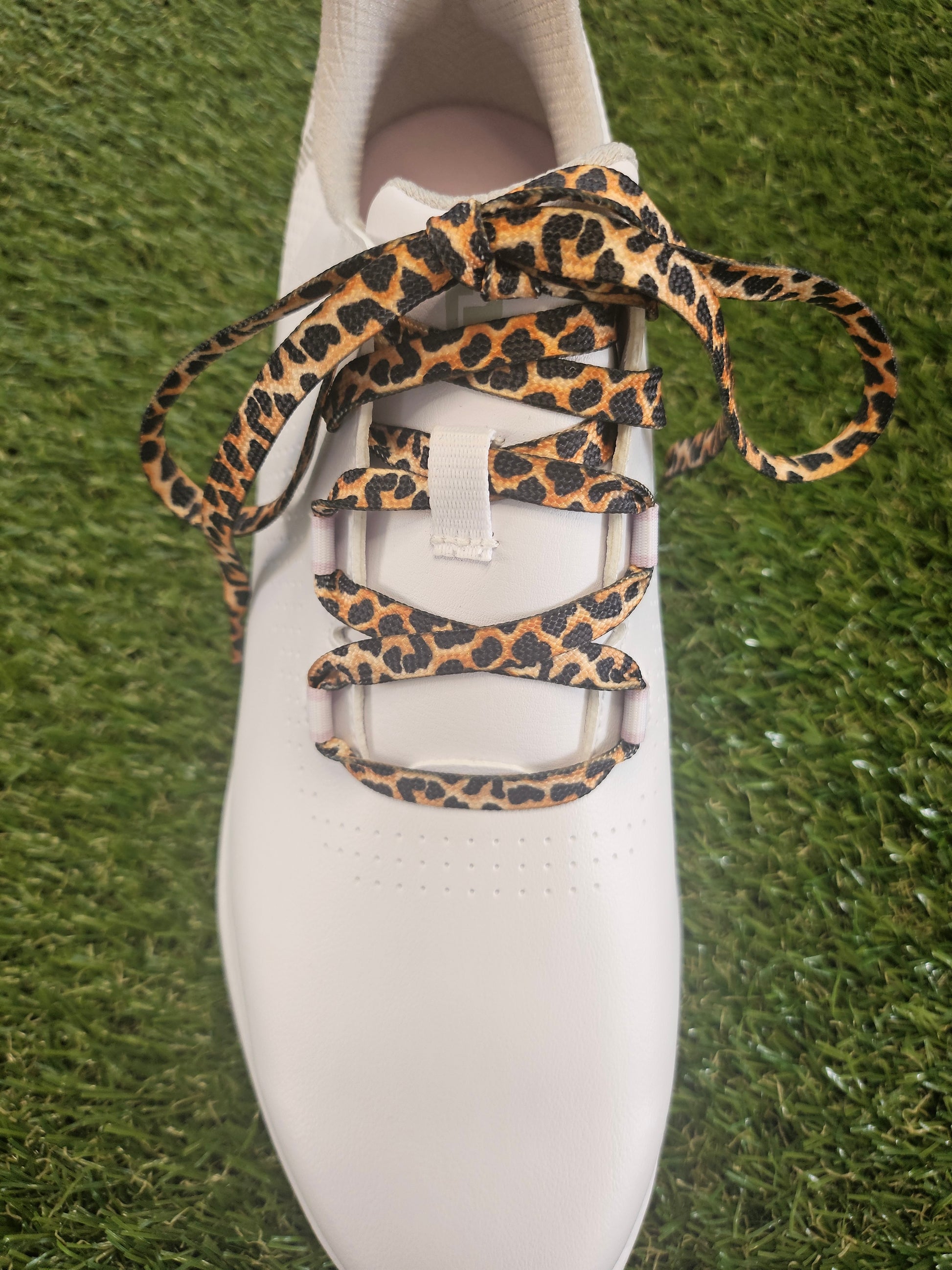 White ladies golf shoe with leopard print laces on a grass background