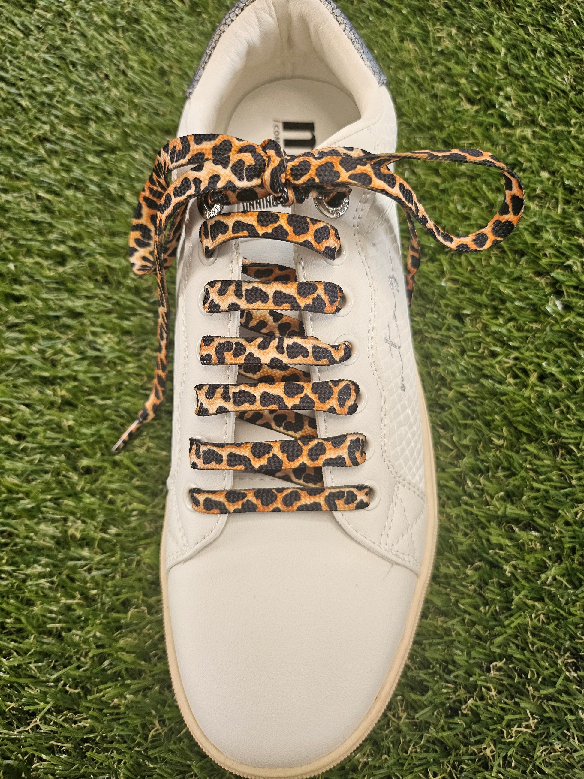 White trainer with leopard print laces on a grass background