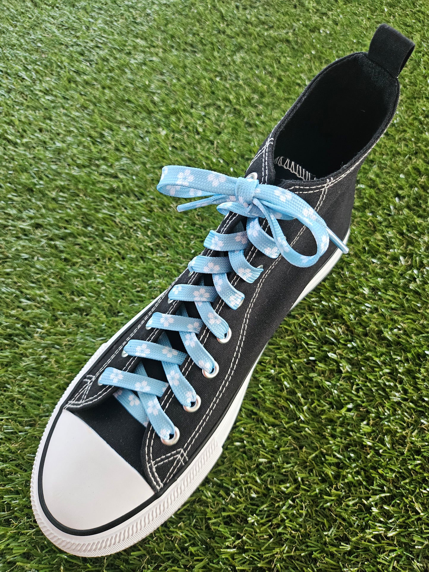 Black high-top sneaker with light blue shoelaces on a grass background