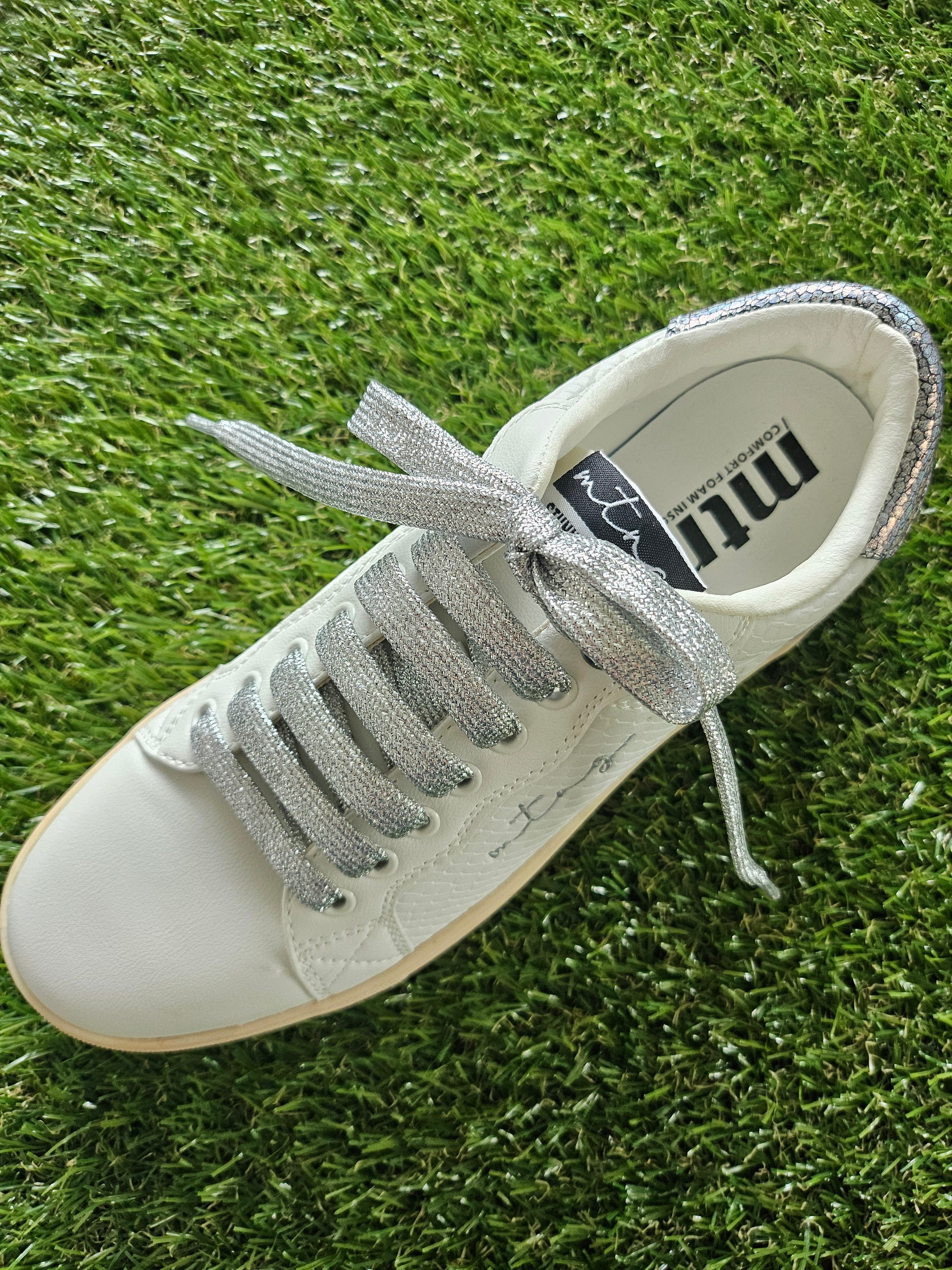 White sneaker with silver laces on a grass background