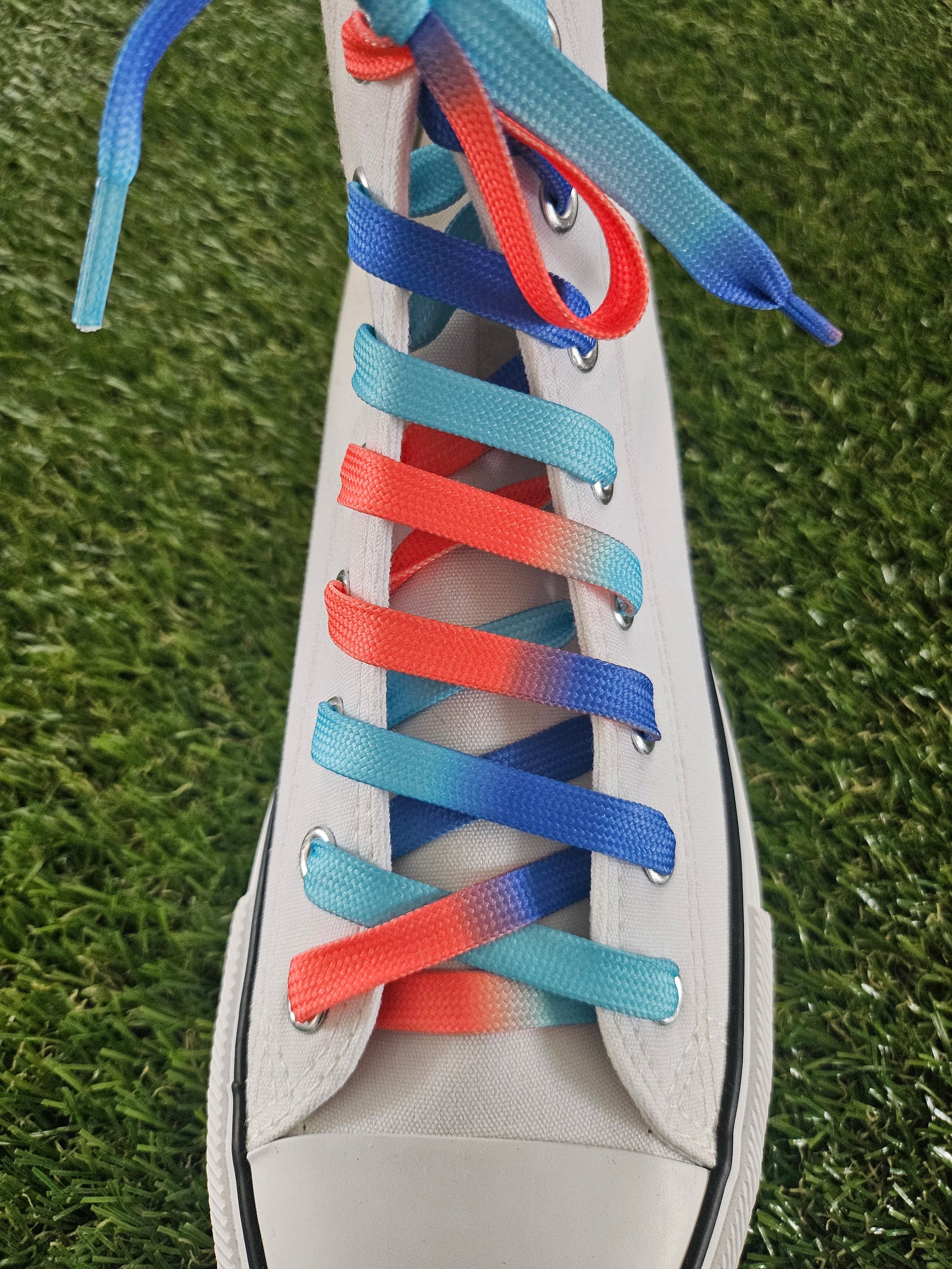 White trainer with gradient blue and coral red shoelaces on a grass background
