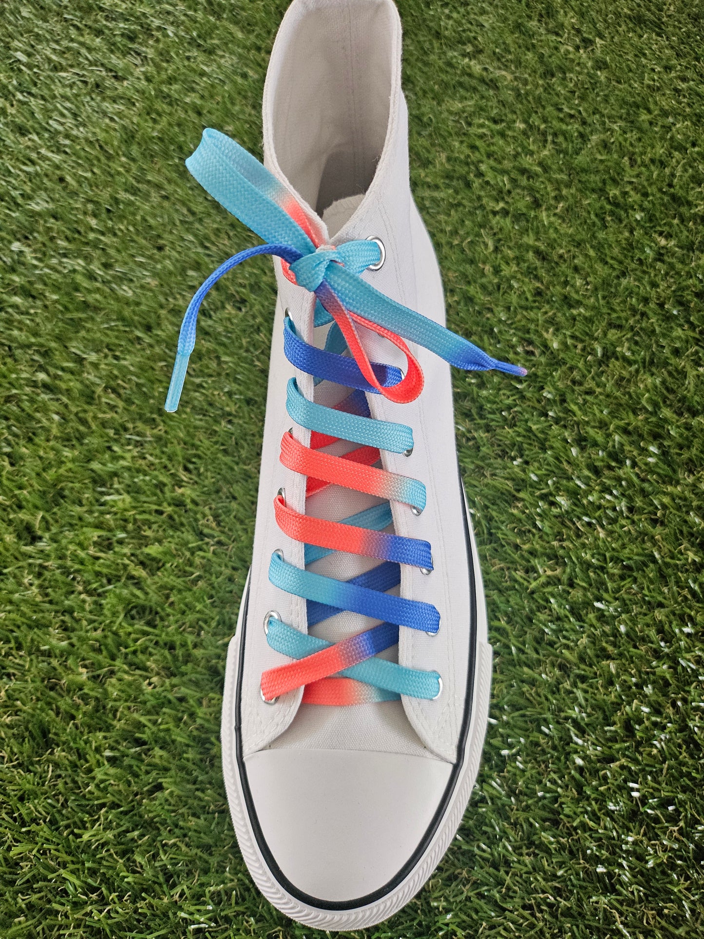 White high top converse boot with colourful shoelaces on a grass background