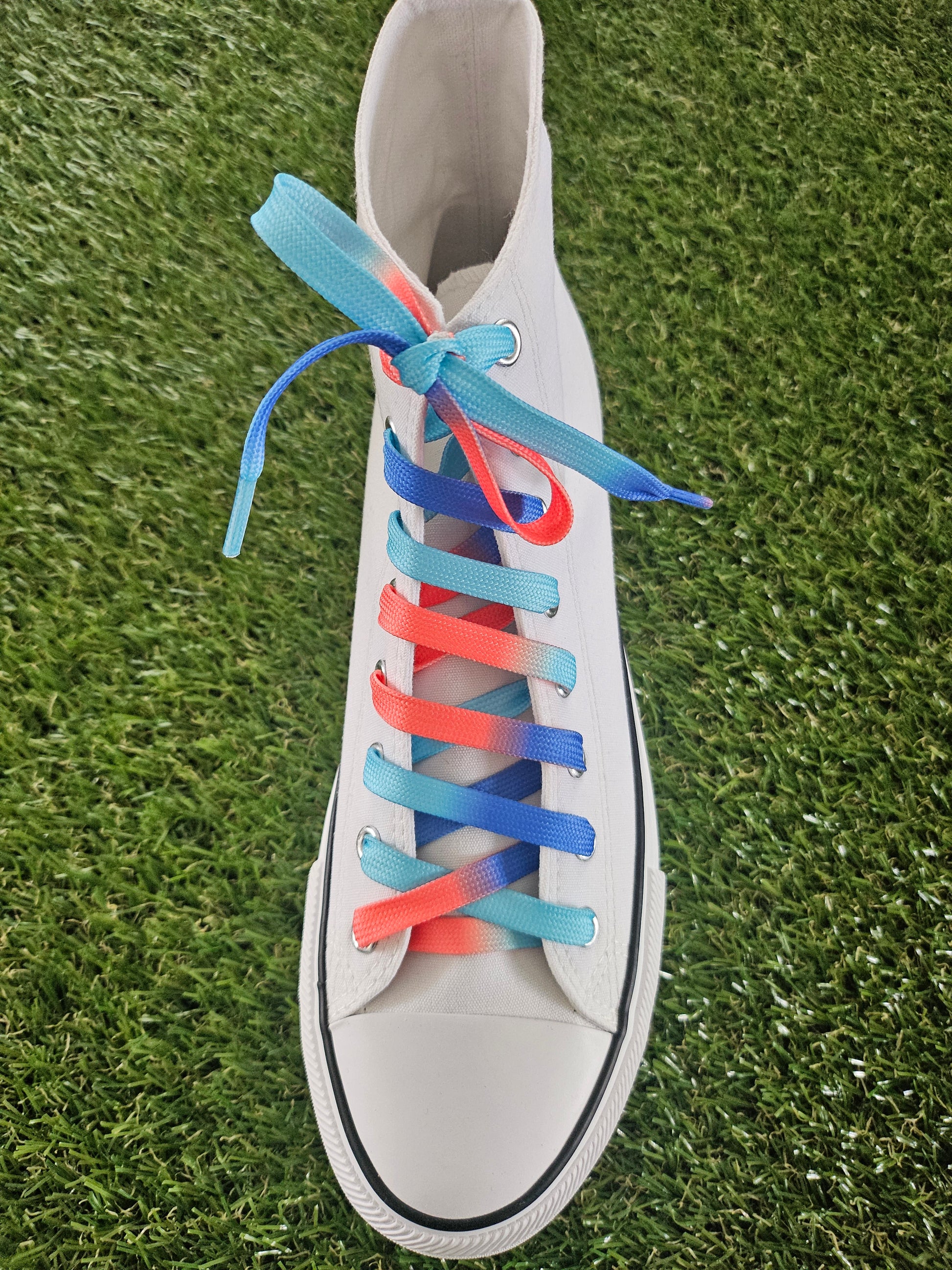 White high top converse boot with colourful shoelaces on a grass background