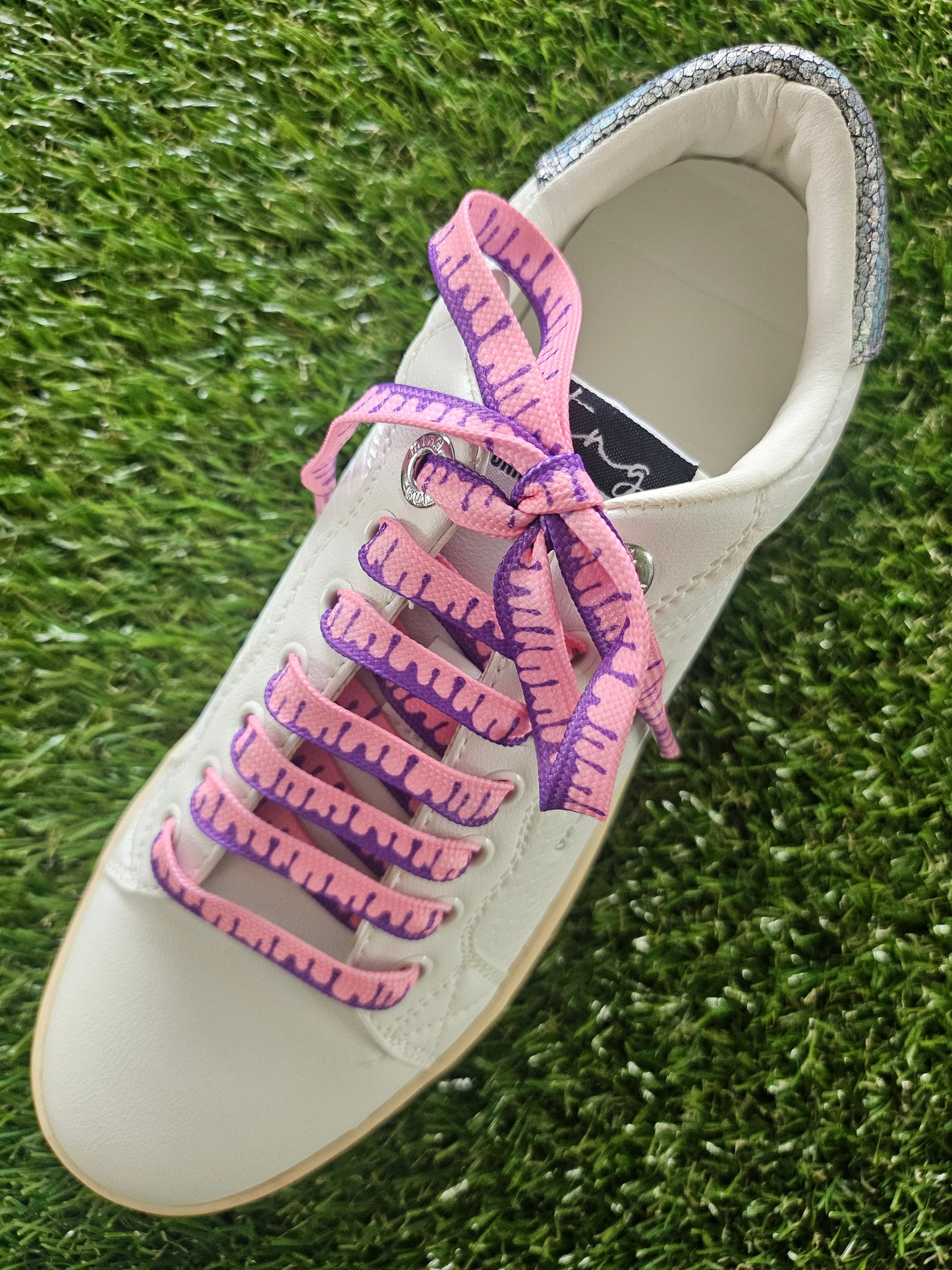 White trainer with pink and purple shoelaces on a grass background