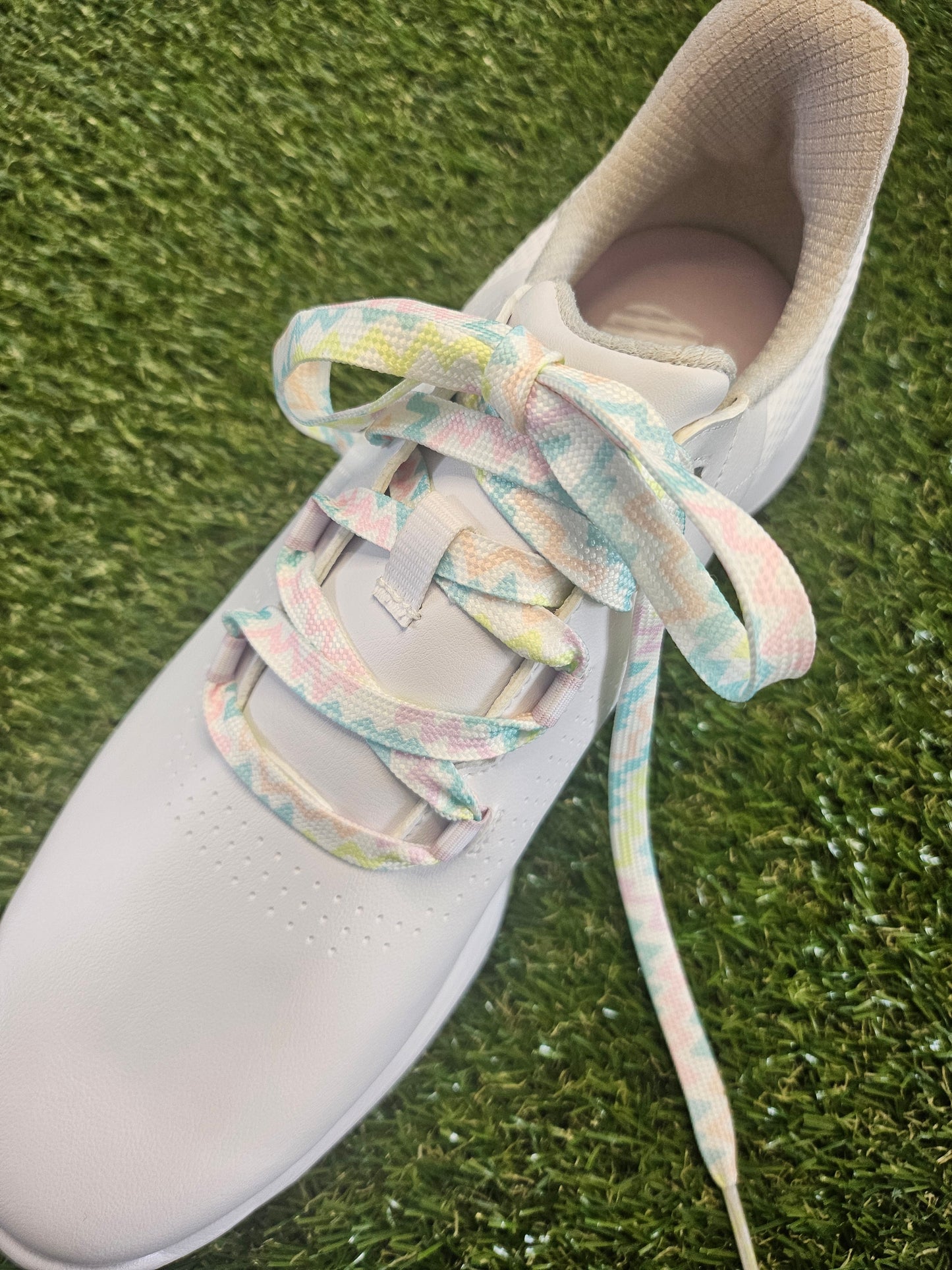 White ladies golf shoe with colourful laces on a grass background