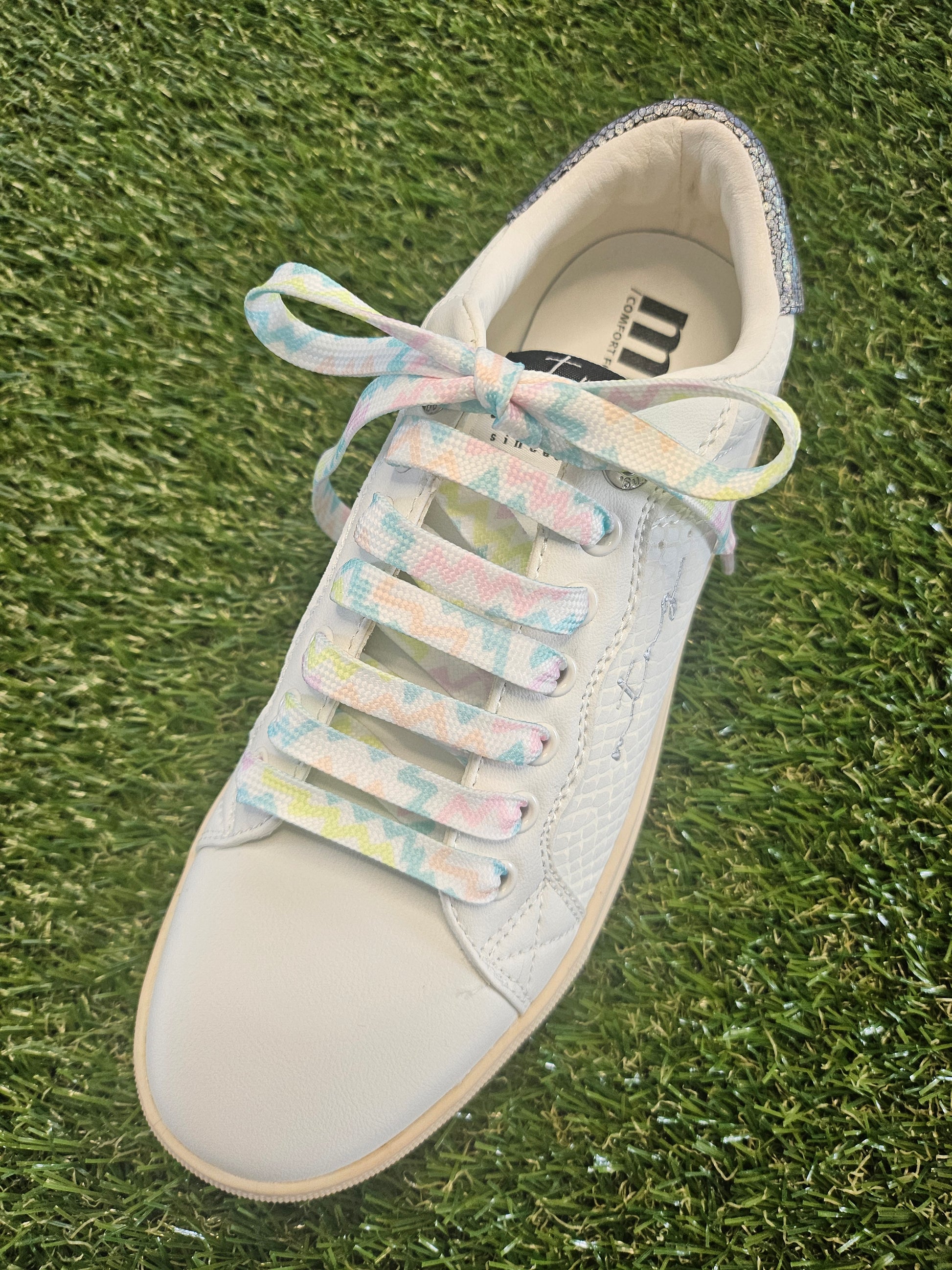 White sneaker with pastel multicolor laces on a grass background