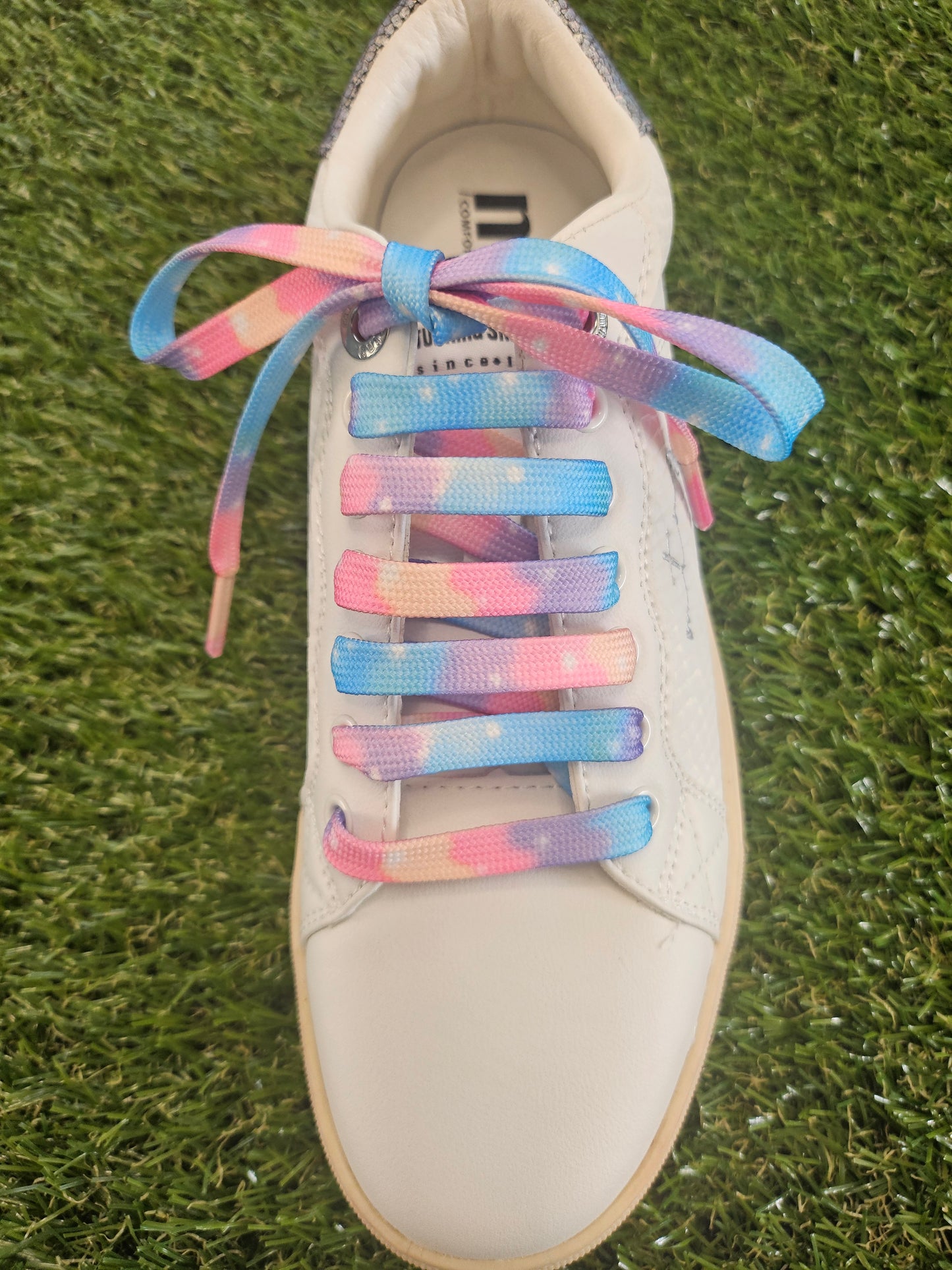 White trainer with cloudy soft  pastel coloured shoelaces on a grass background