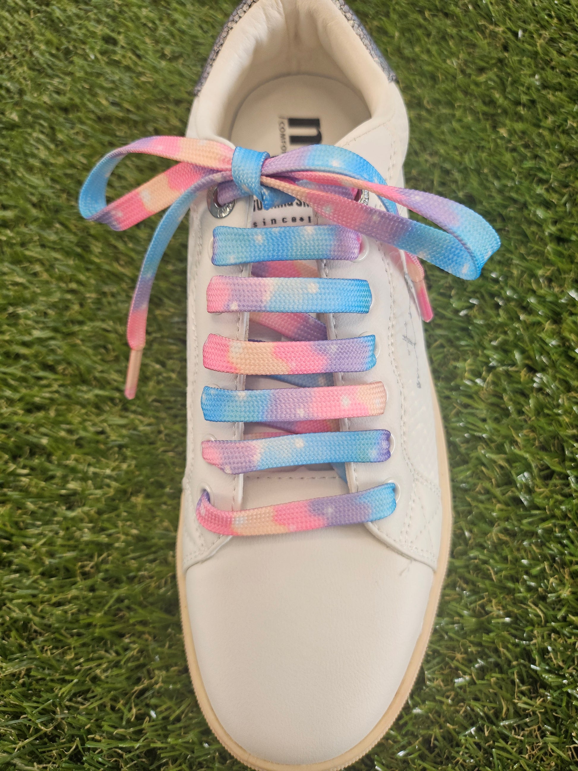 White trainer with cloudy soft  pastel coloured shoelaces on a grass background