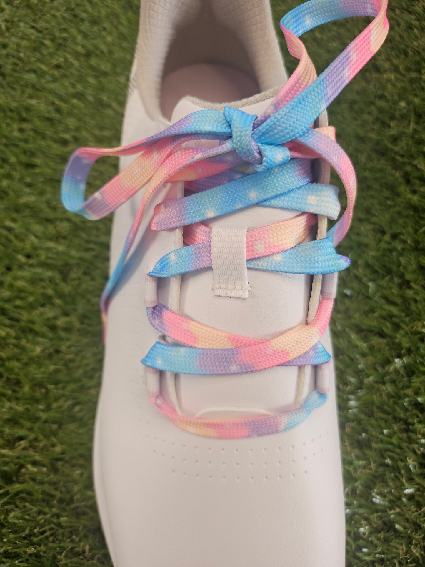 Ladies white golf shoe with colourful cloudy soft  pastel coloured shoelaces on a grass background