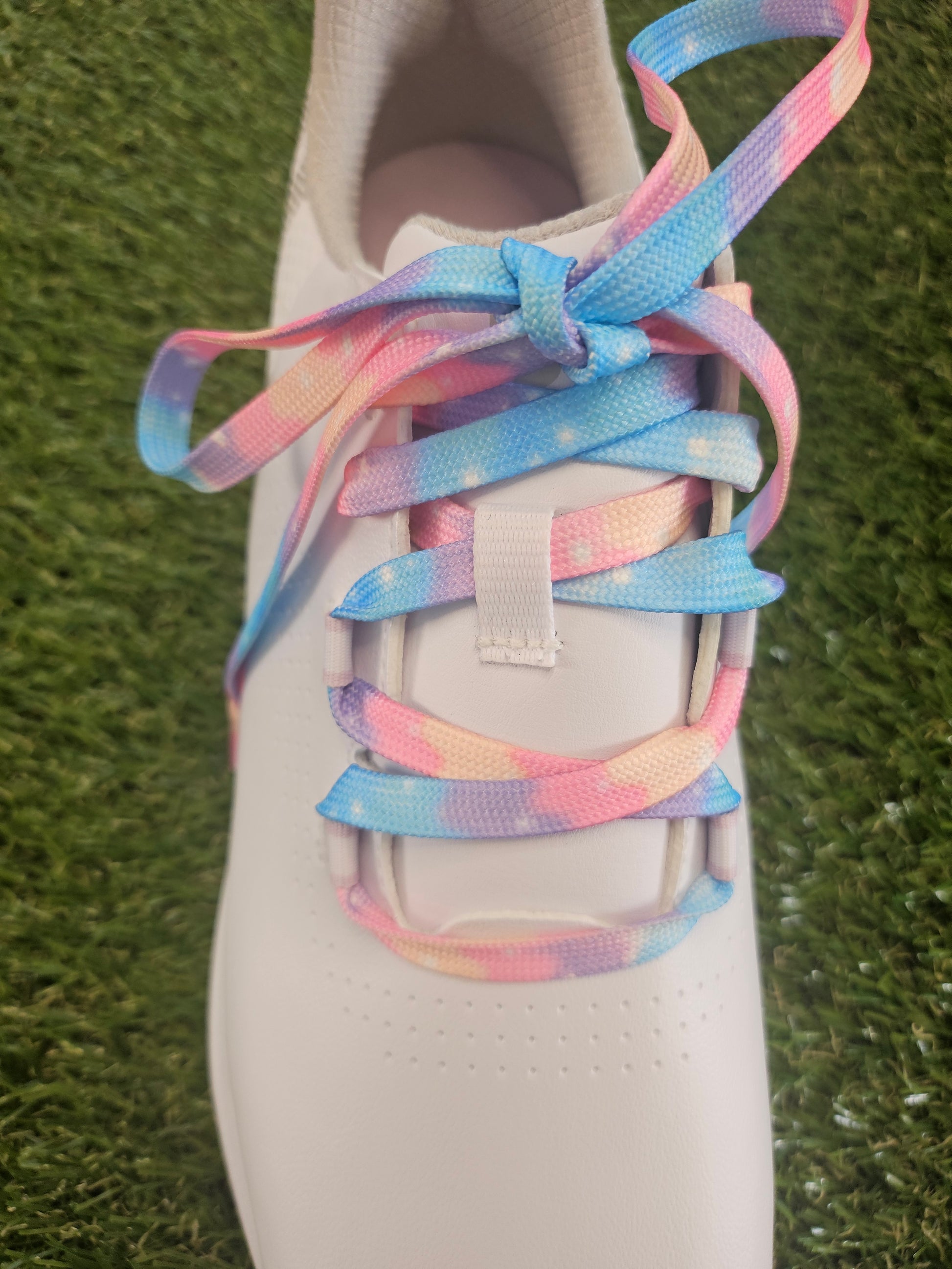 Ladies white golf shoe with colourful cloudy soft  pastel coloured shoelaces on a grass background