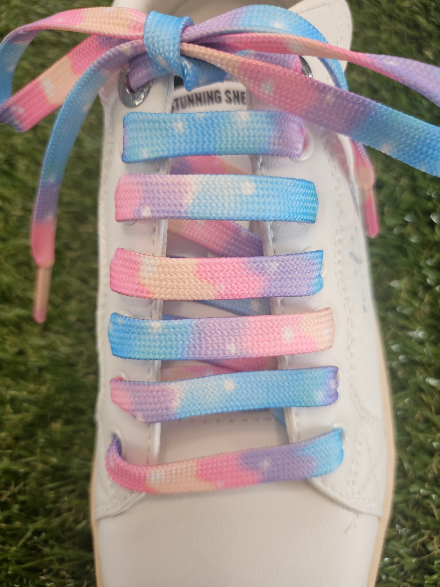 White trainer with colourful cloudy soft  pastel coloured shoelaces on a grass background
