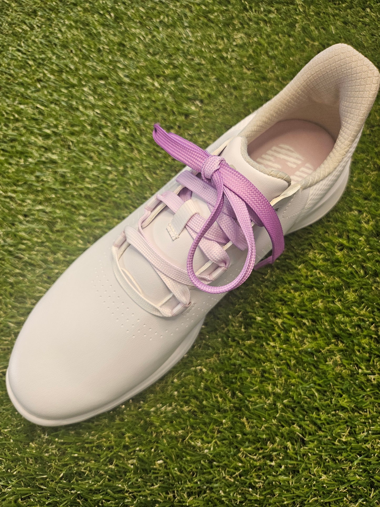 White golf shoes with purple fade laces on grass