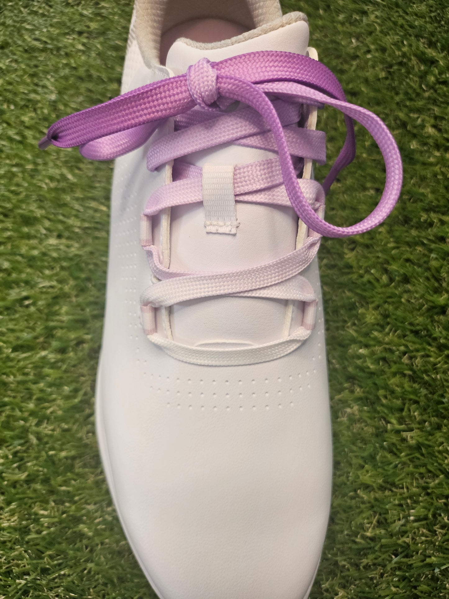 White ladies golf shoe with purple fade laces on a grass background