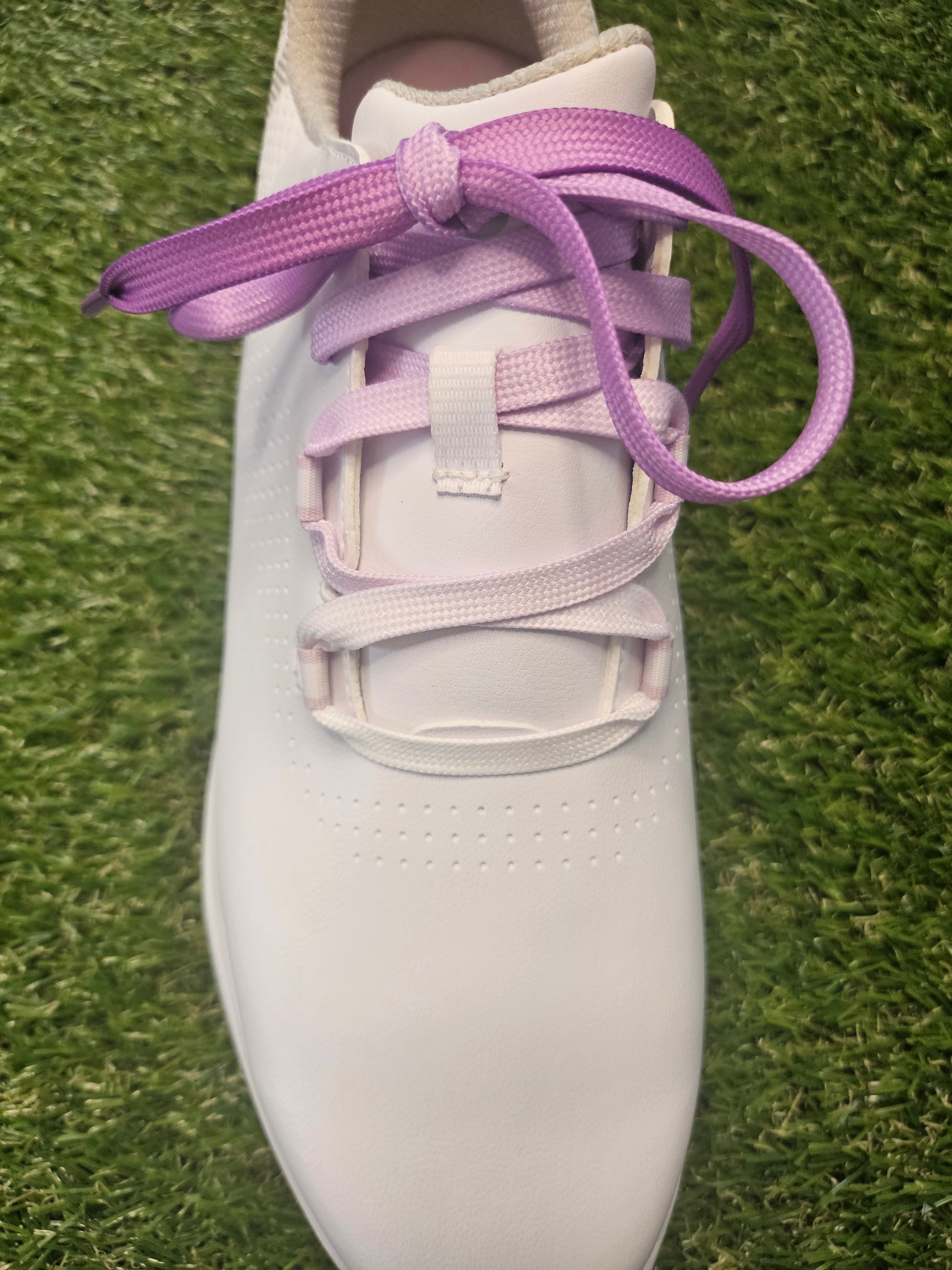 White ladies golf shoe with purple fade laces on a grass background