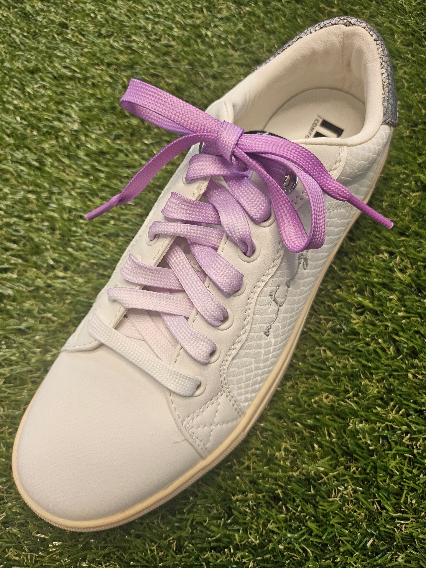 White sneaker with purple fade laces on a grass background