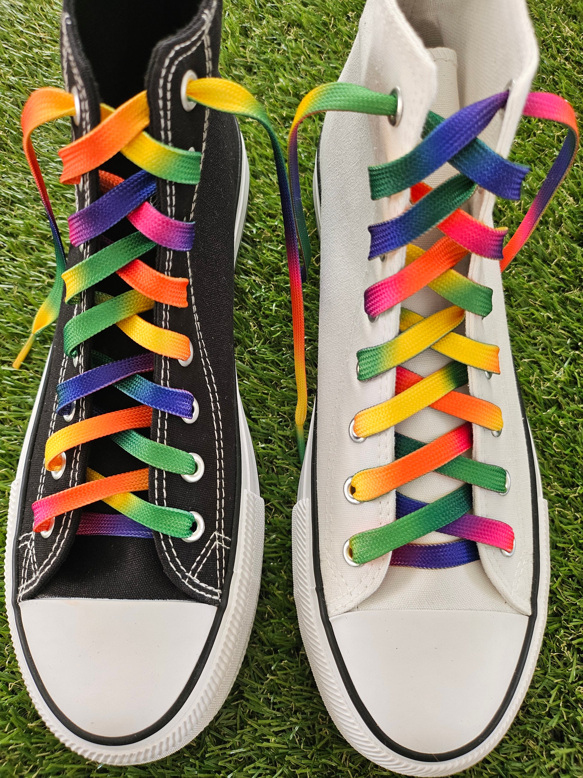 White and black converse boots with colourful rainbow laces on a grass background