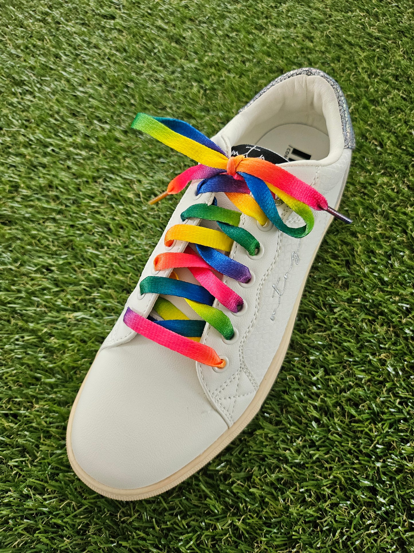 White trainer with rainbow laces on a grass background
