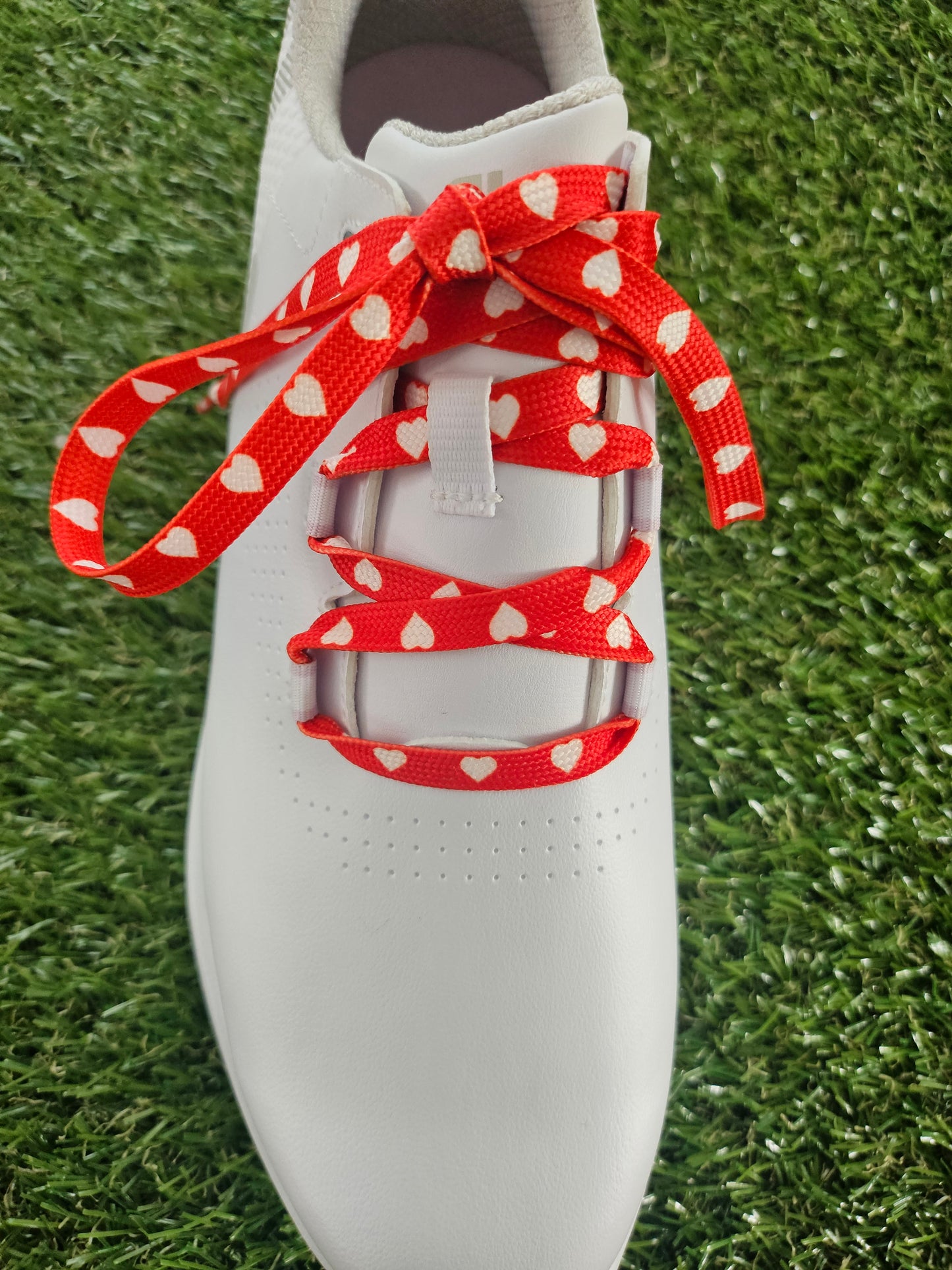 White golf shoe with red shoelaces featuring white heart patterns on a grass background