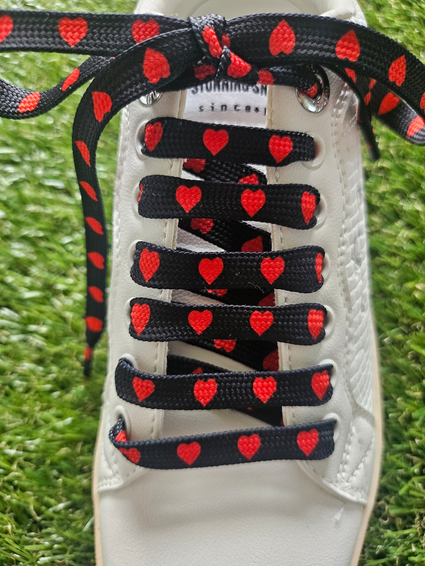 Shoe with black laces featuring red heart patterns on a grass background
