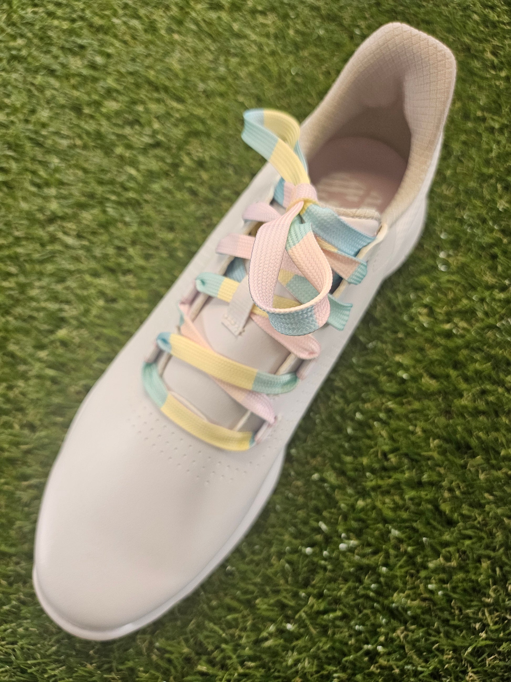 White womans golf shoe with pale coloured shoelaces on a grass background
