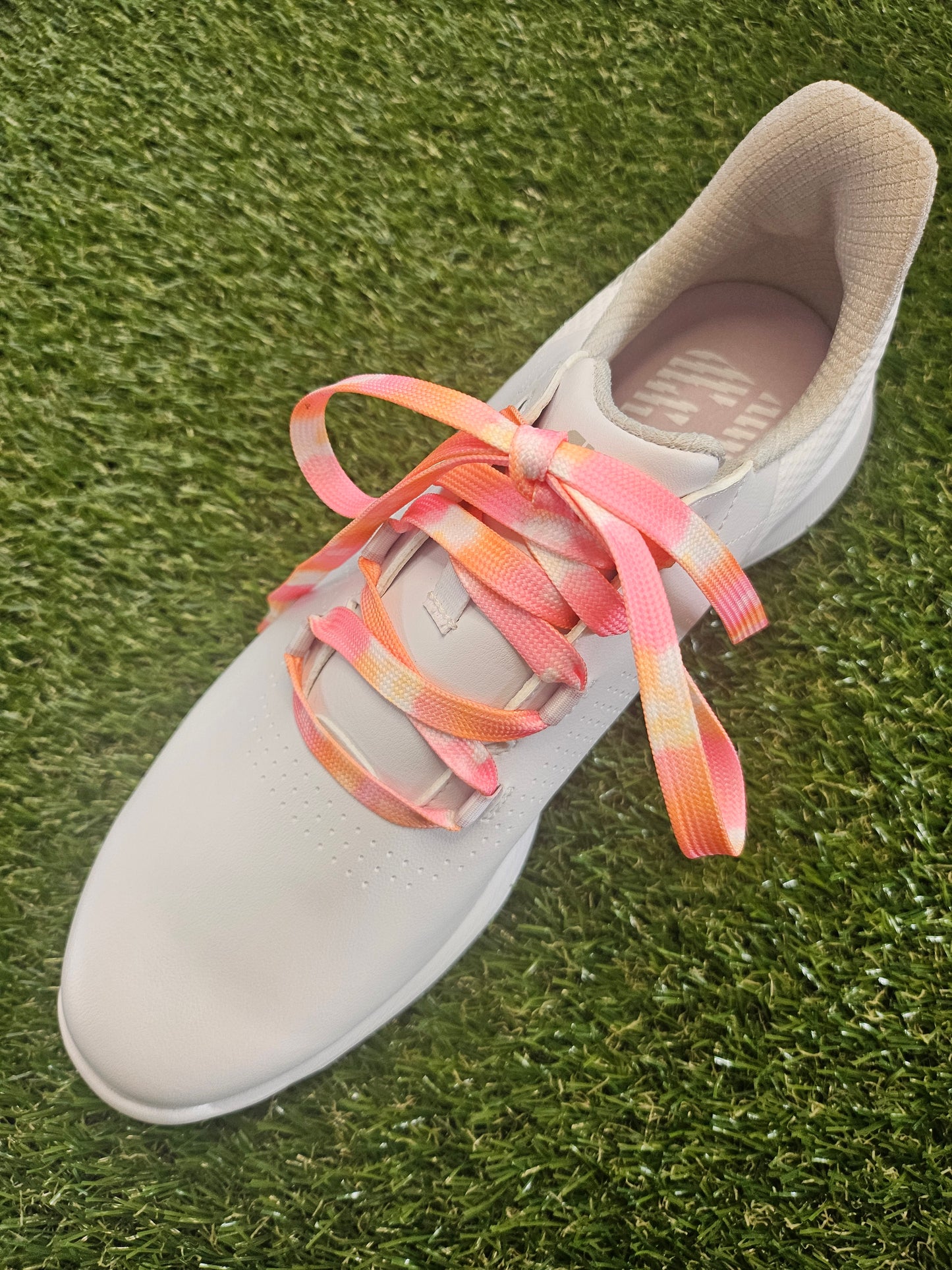 White female golf shoe with peach coloured shoelaces on a grass background