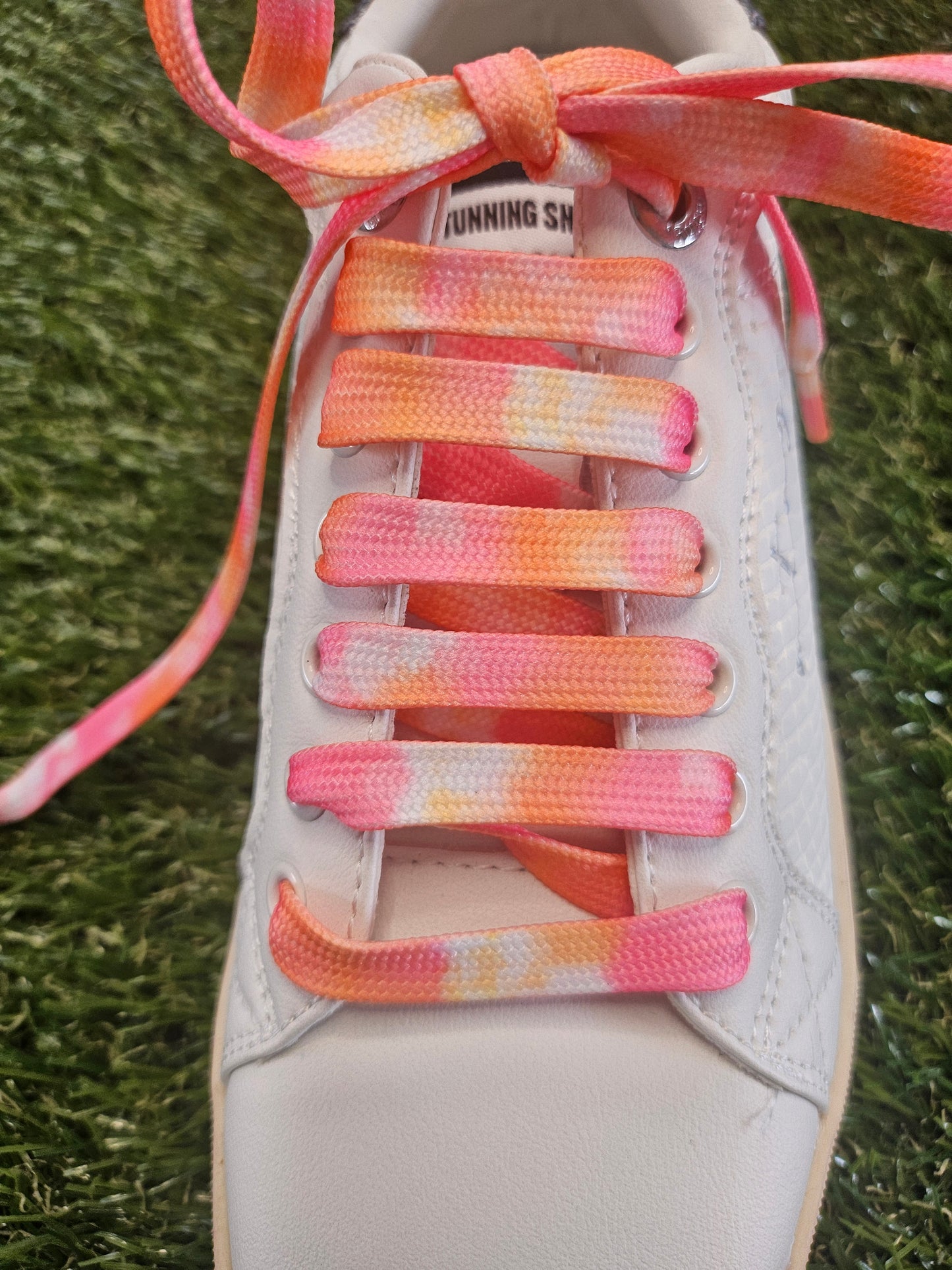 White trainer with colourful shoelaces on a grass background