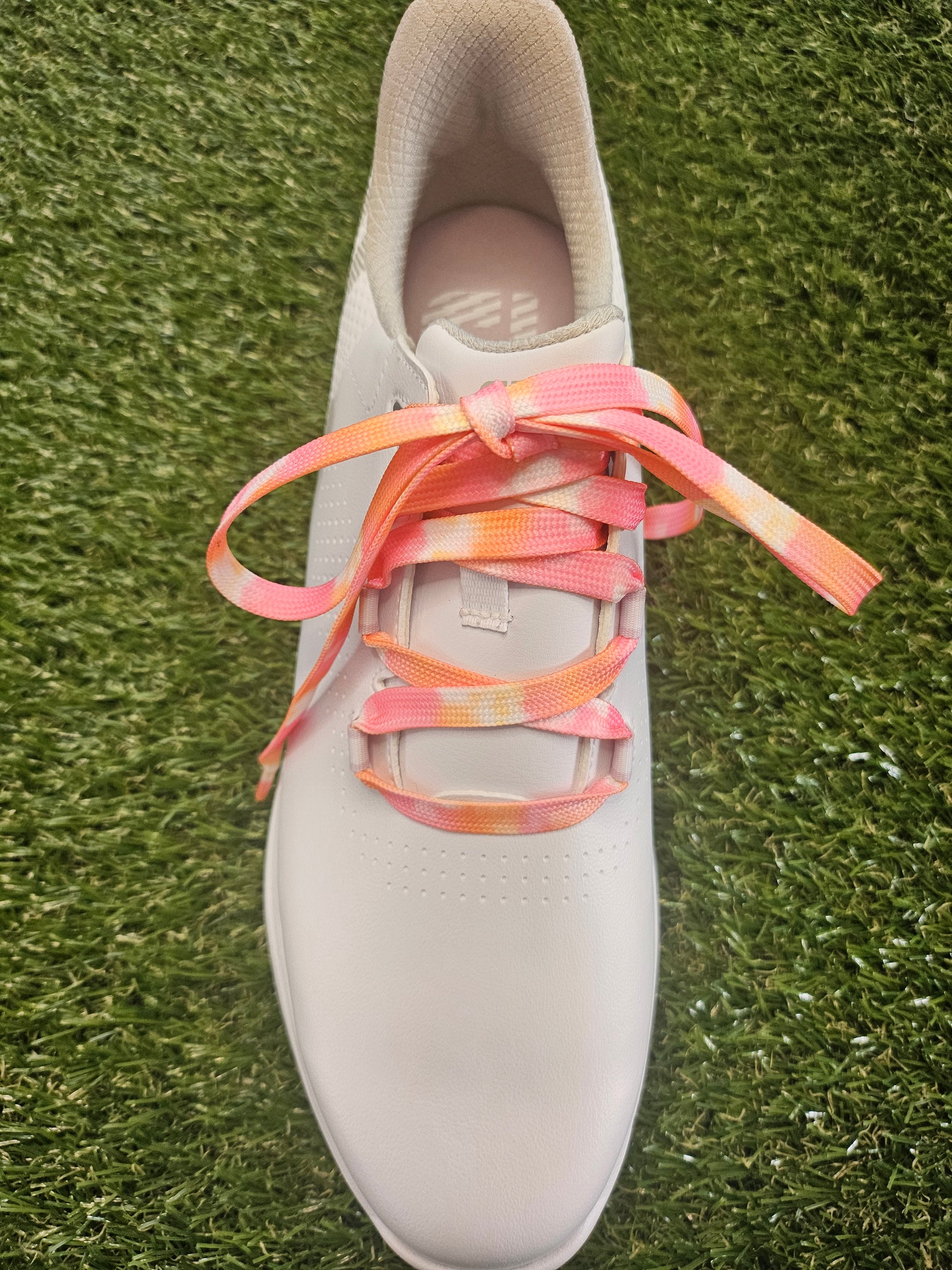White ladies golf shoe with pink and orange laces on a grass background