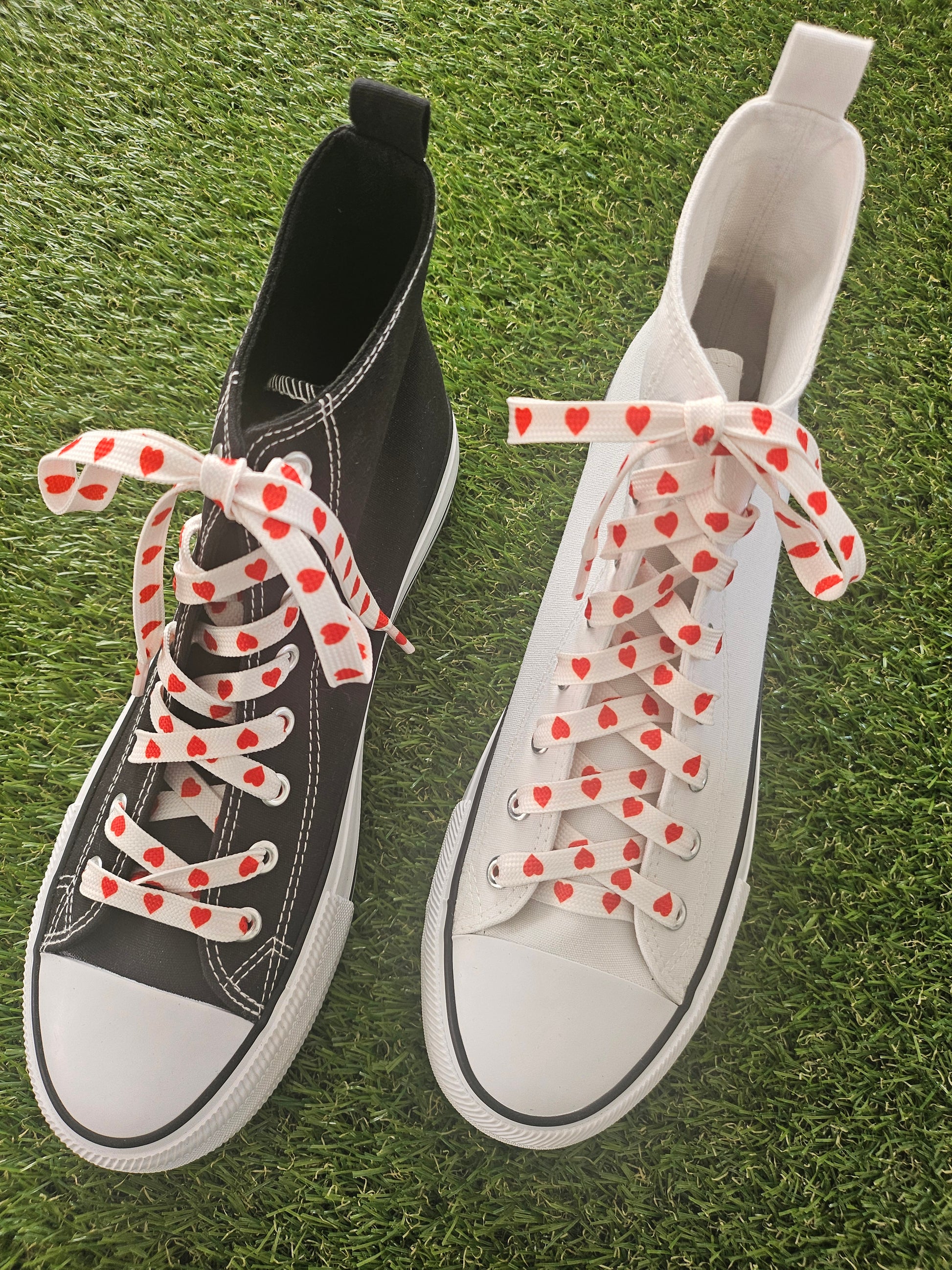Black and white sneakers with red heart patterns on laces on grass