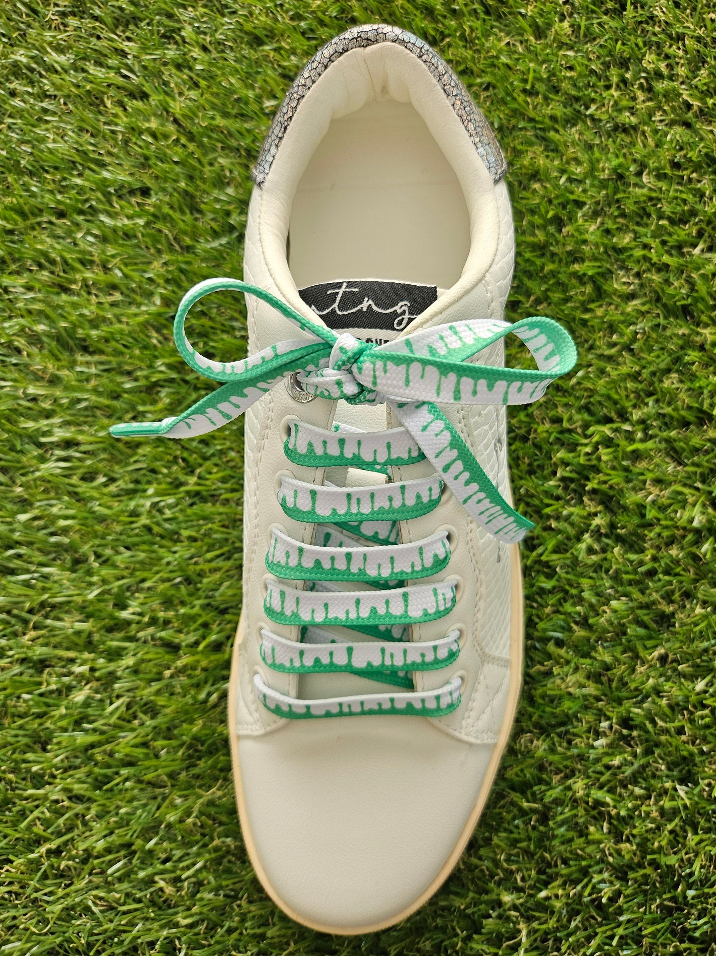 White sneaker with green laces on grass
