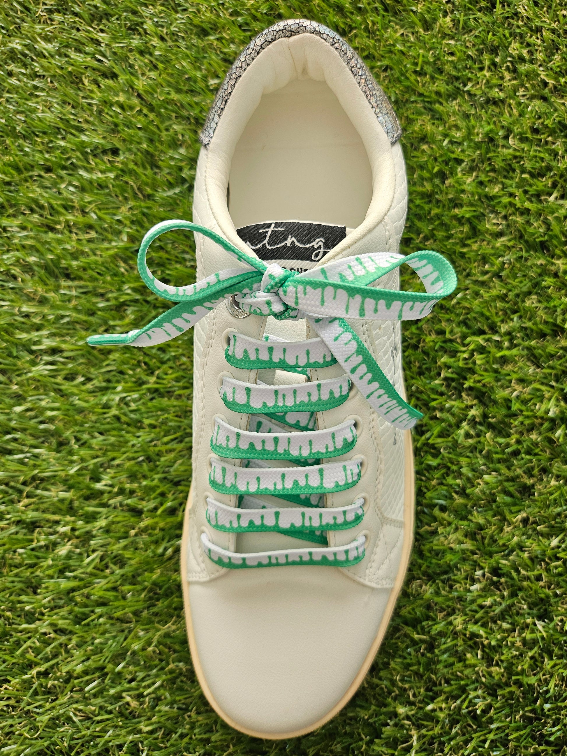 White sneaker with green laces on grass