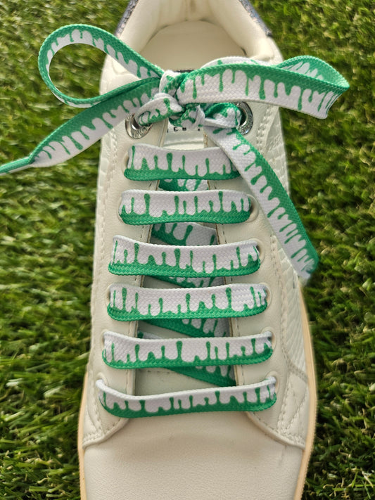 Close-up of a shoe with green and white patterned laces on grass.