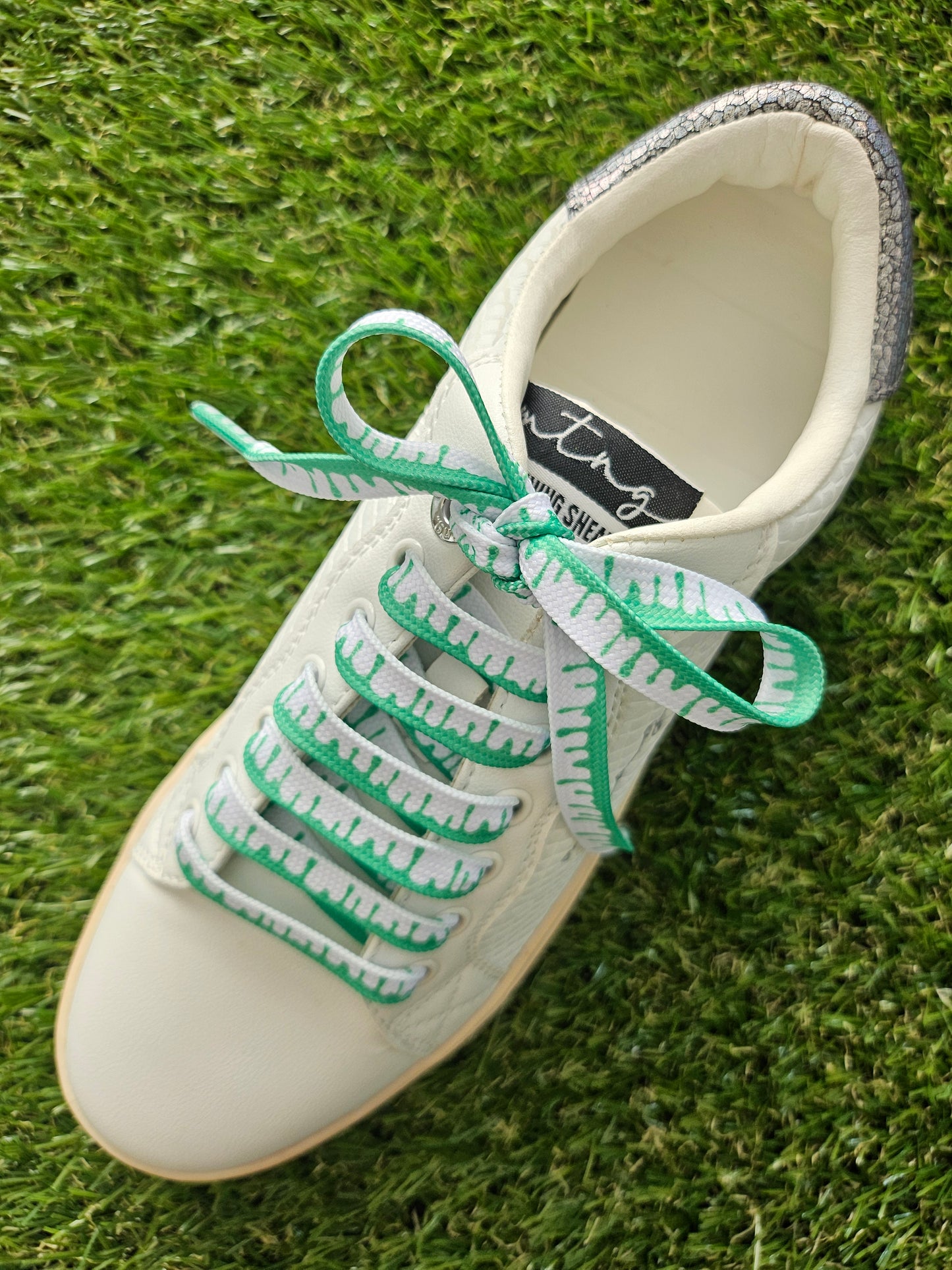 White sneaker with green laces on a grass background
