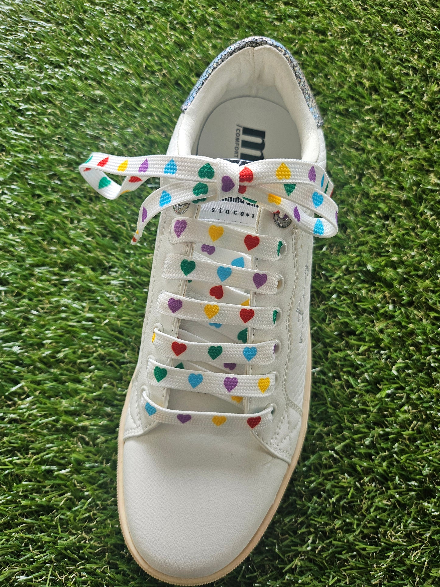 White sneaker with colorful laces on grass