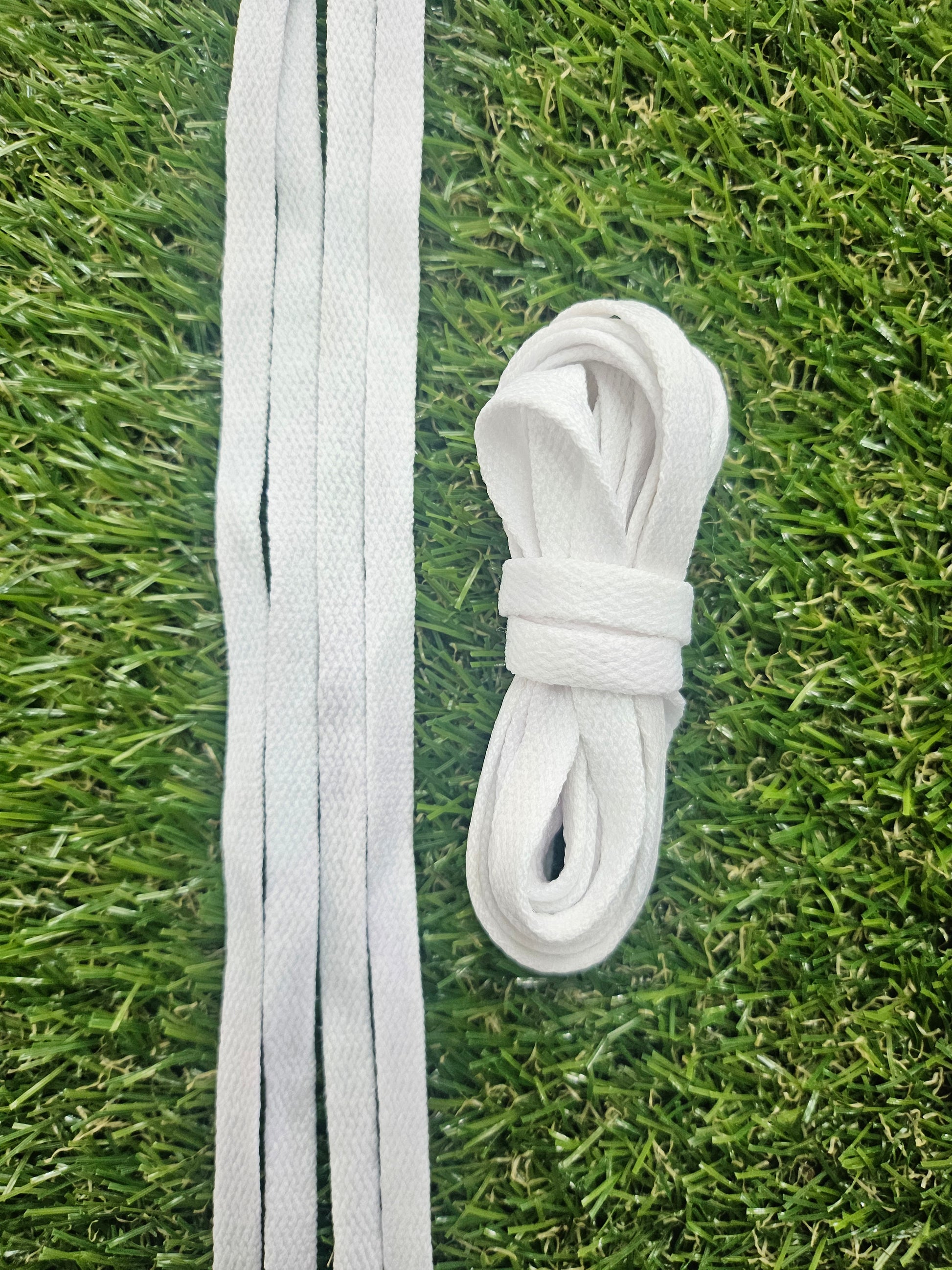 A coiled bundle of white shoelaces placed on green artificial grass, with several loose shoelaces extending horizontally across the foreground.