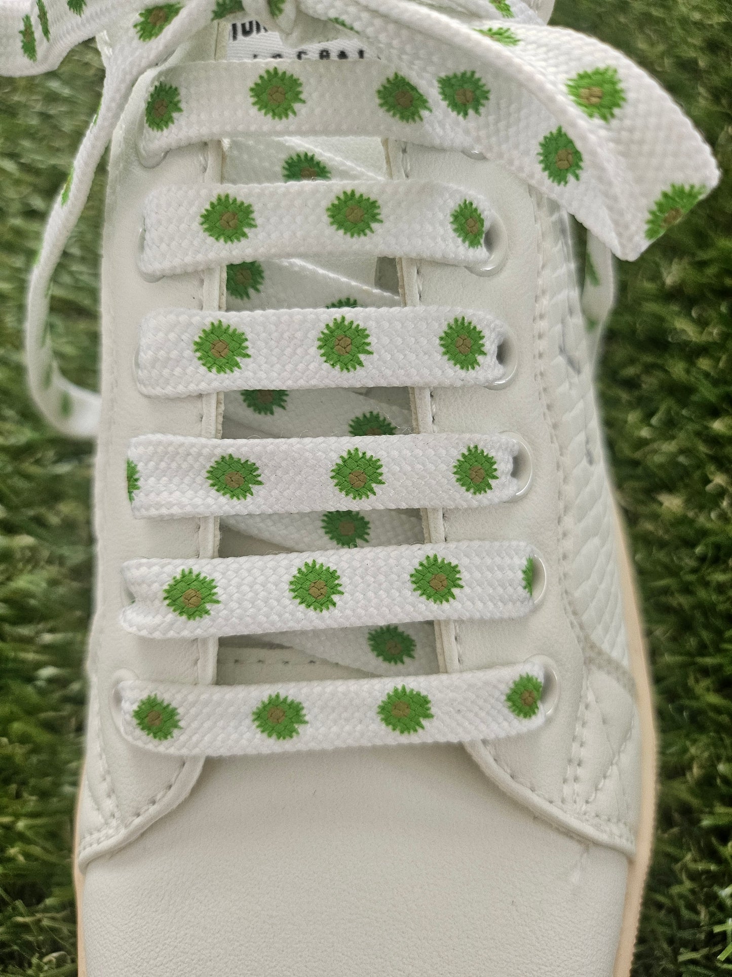 White trainer with green floral patterns on laces against a grass background