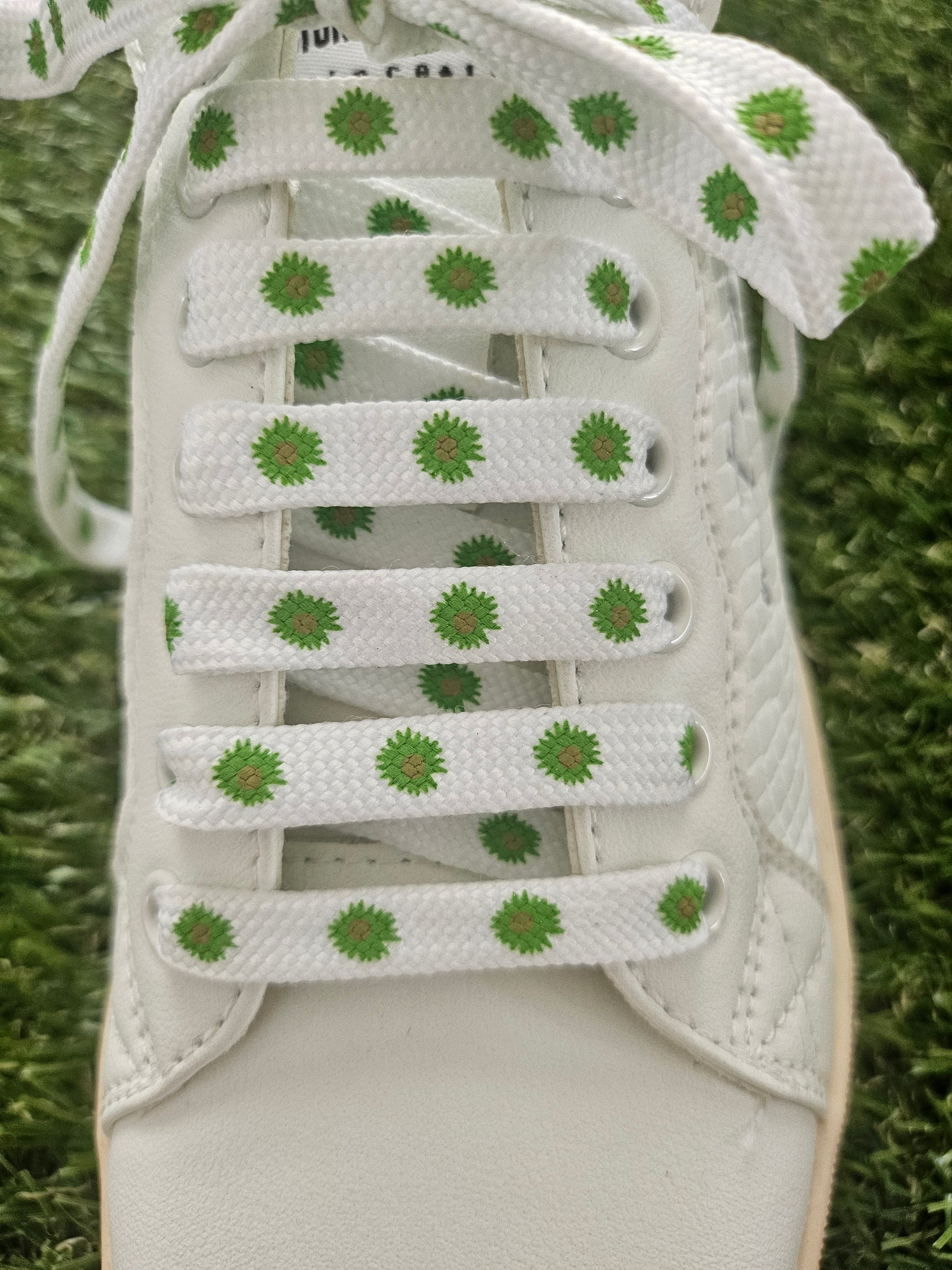 White trainer with green floral patterns on laces against a grass background