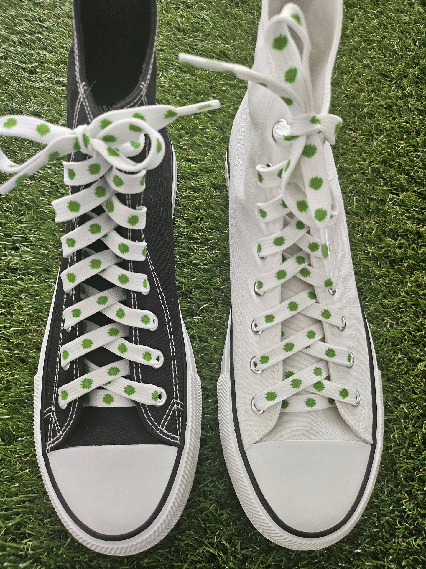 White and a black converse boot with green flowers on white laces on a grass background
