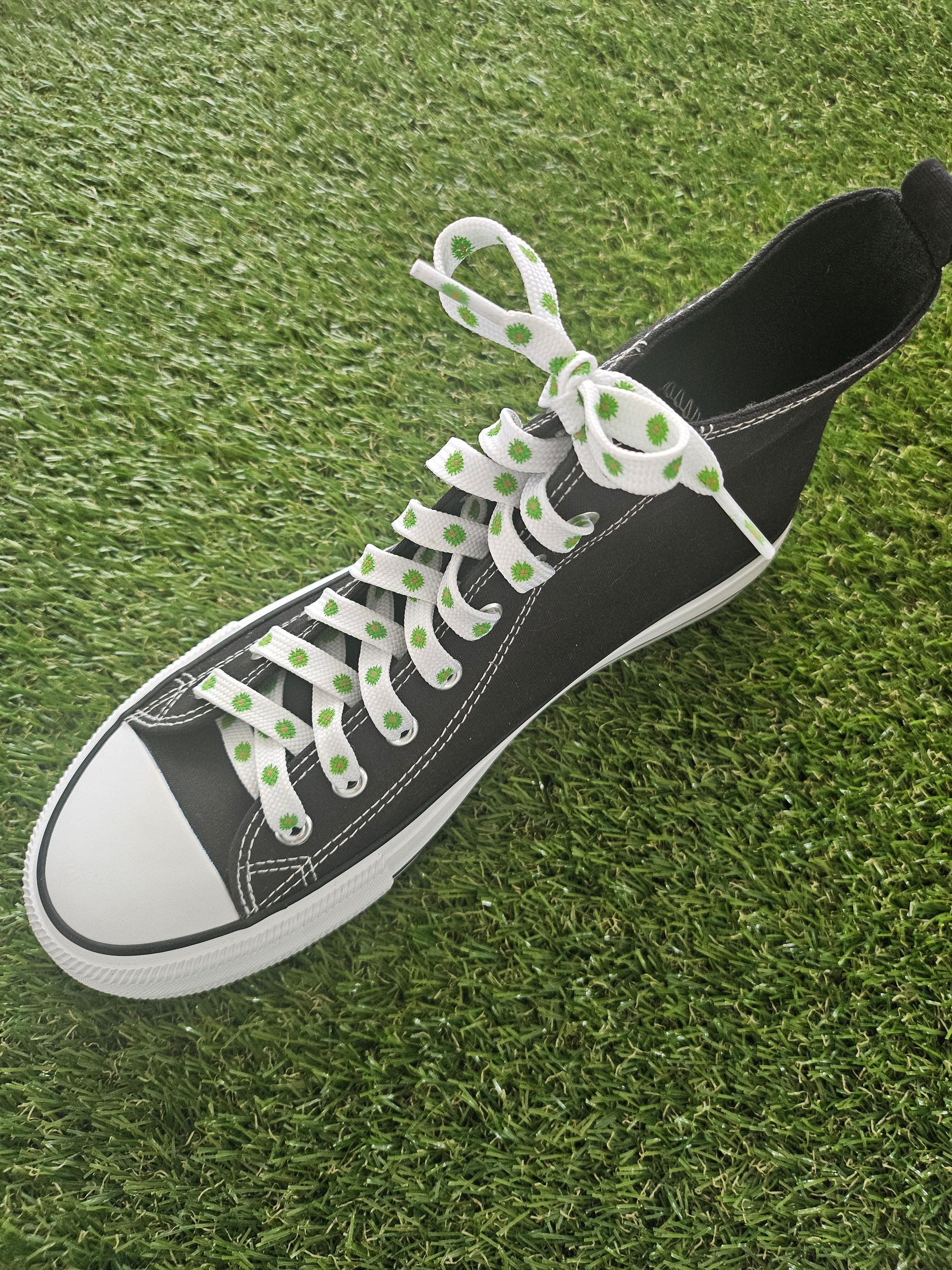 Black sneaker with white laces with green flowers on a grass background
