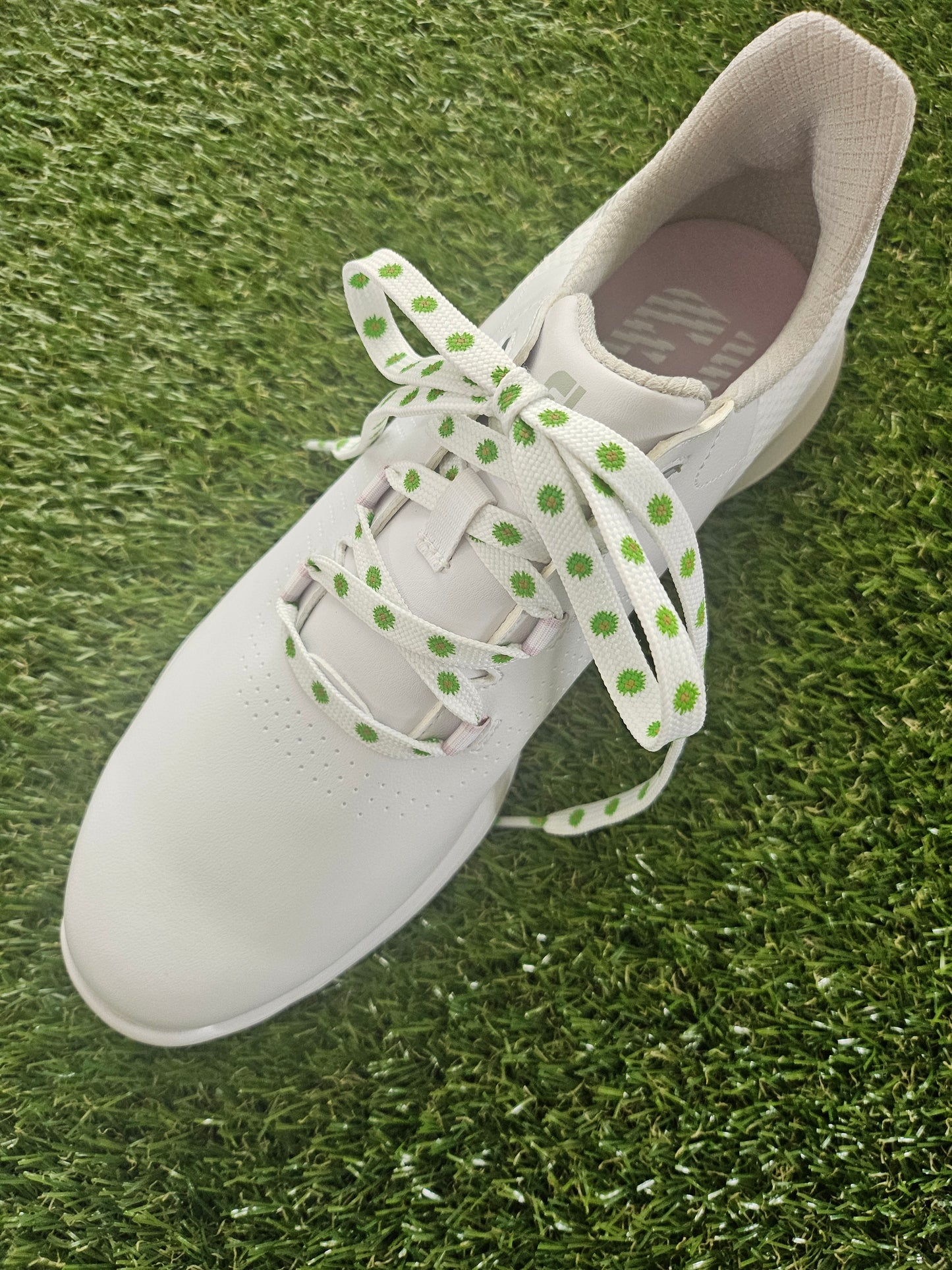 White ladies golf shoe with green flowers on white laces on grass