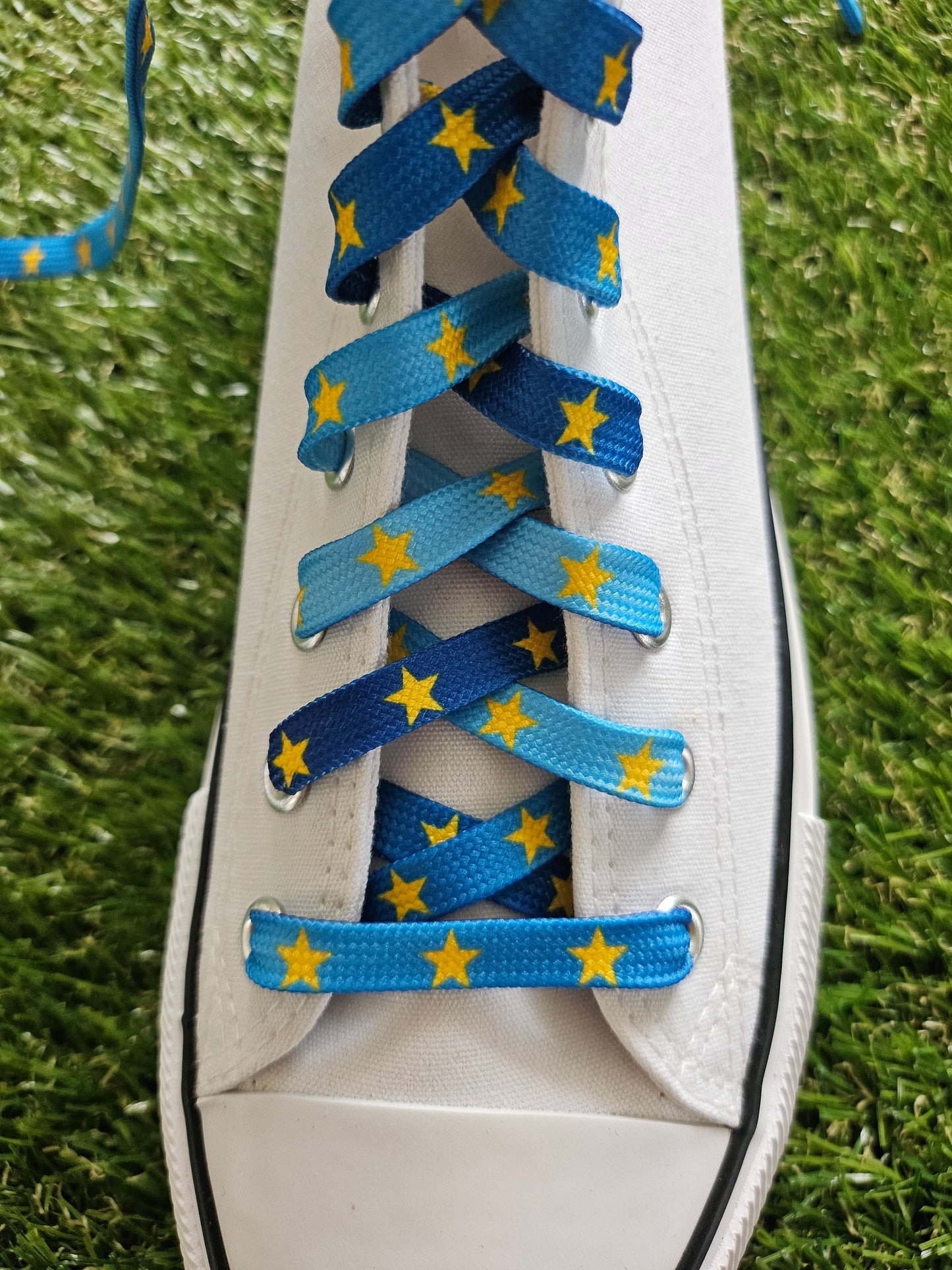 White converse sneaker with blue shoelaces featuring yellow stars on a grass background