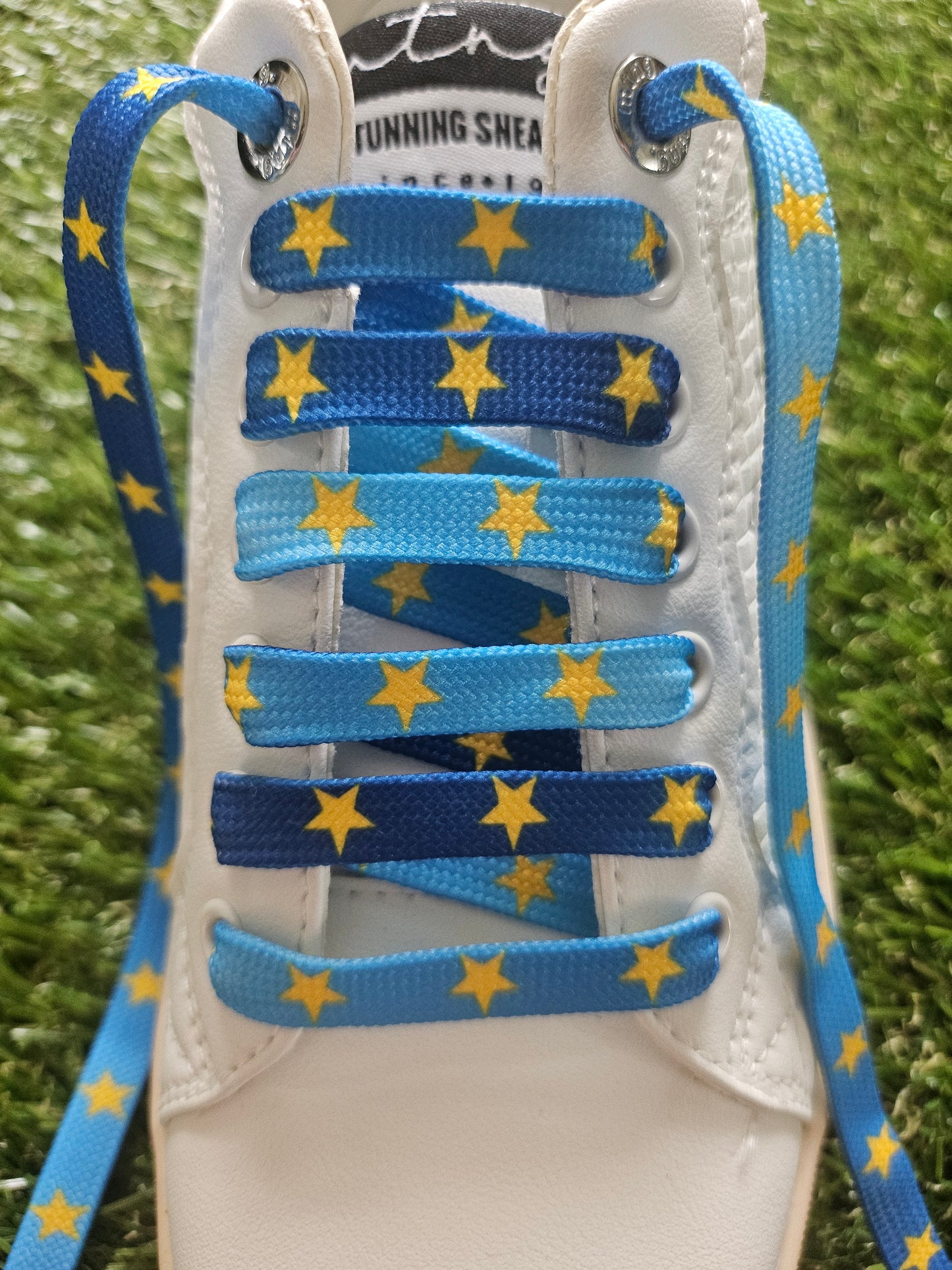 White traineer with blue shoelaces featuring yellow stars on a grass background